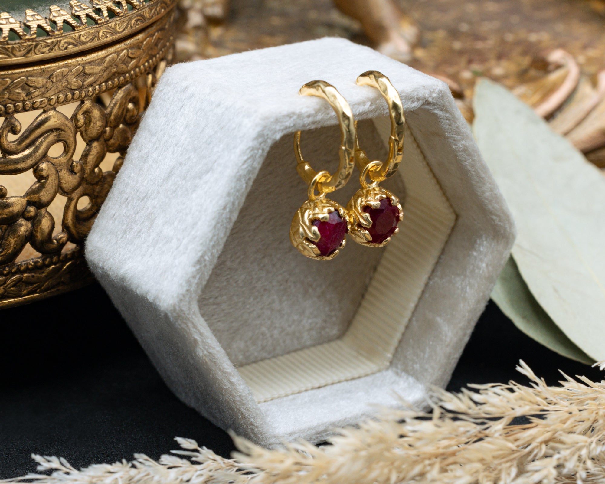 Gold earrings with red rubies in a jewelry box on a textured surface