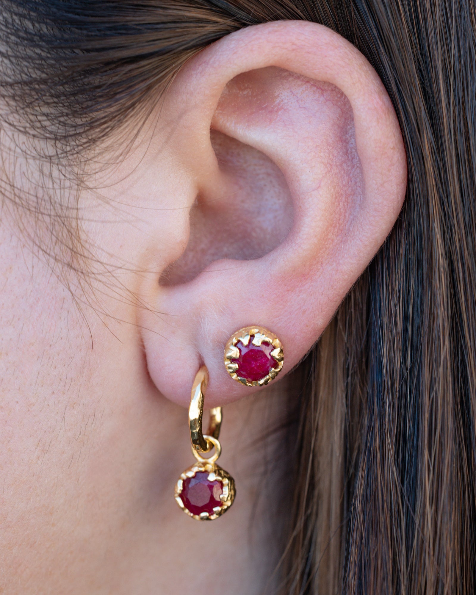 Gold earrings with red rubies worn by a person