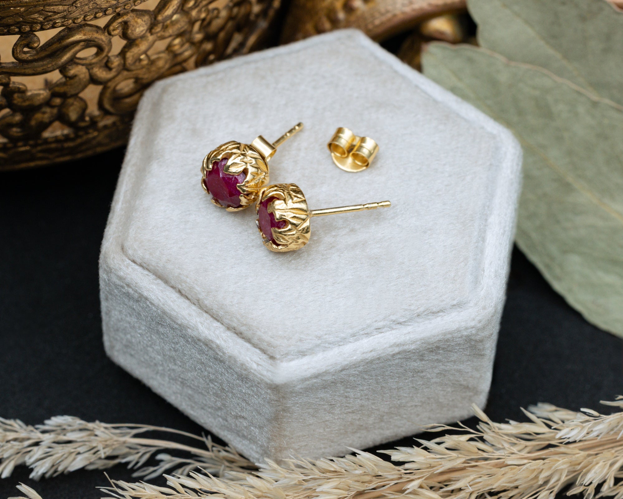 Gold earrings with red rubies on a hexagonal white pillow.