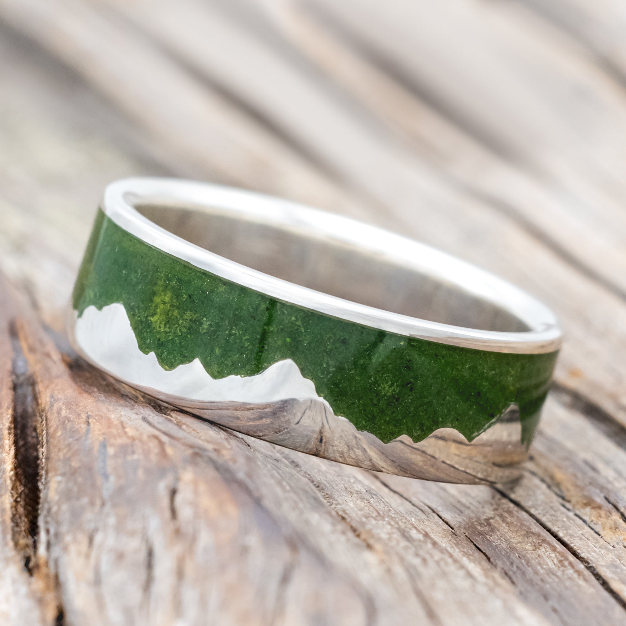 Silver ring with moss inlay and mountain range design on a wooden surface