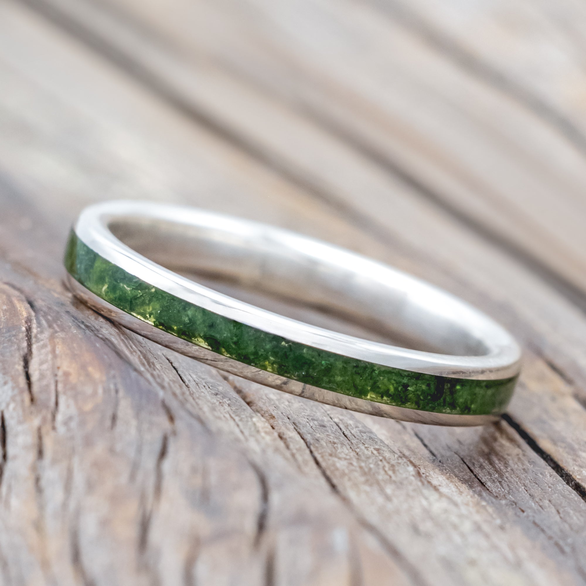 Silver ring with moss inlay on a wooden surface