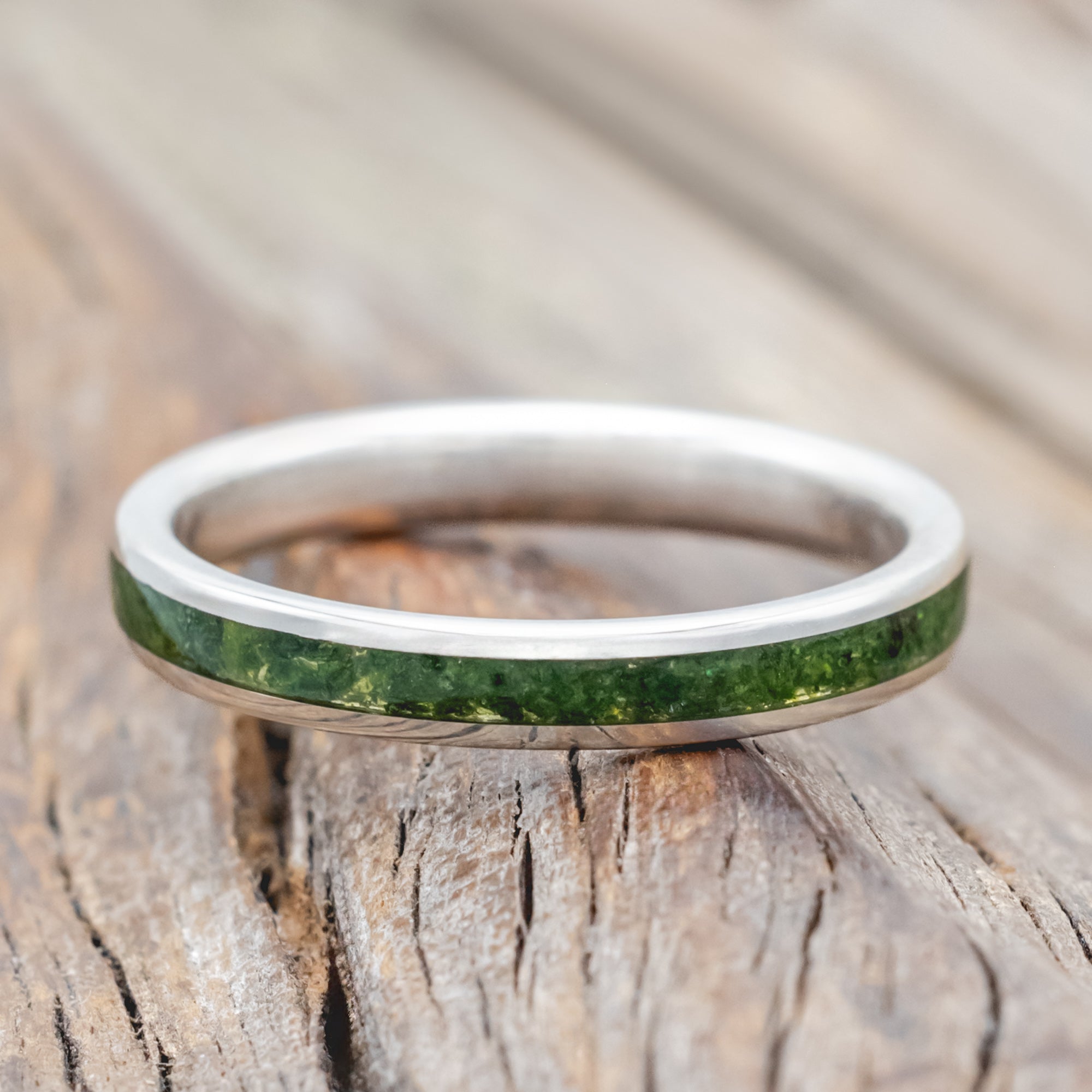Silver ring with moss inlay on a wooden surface