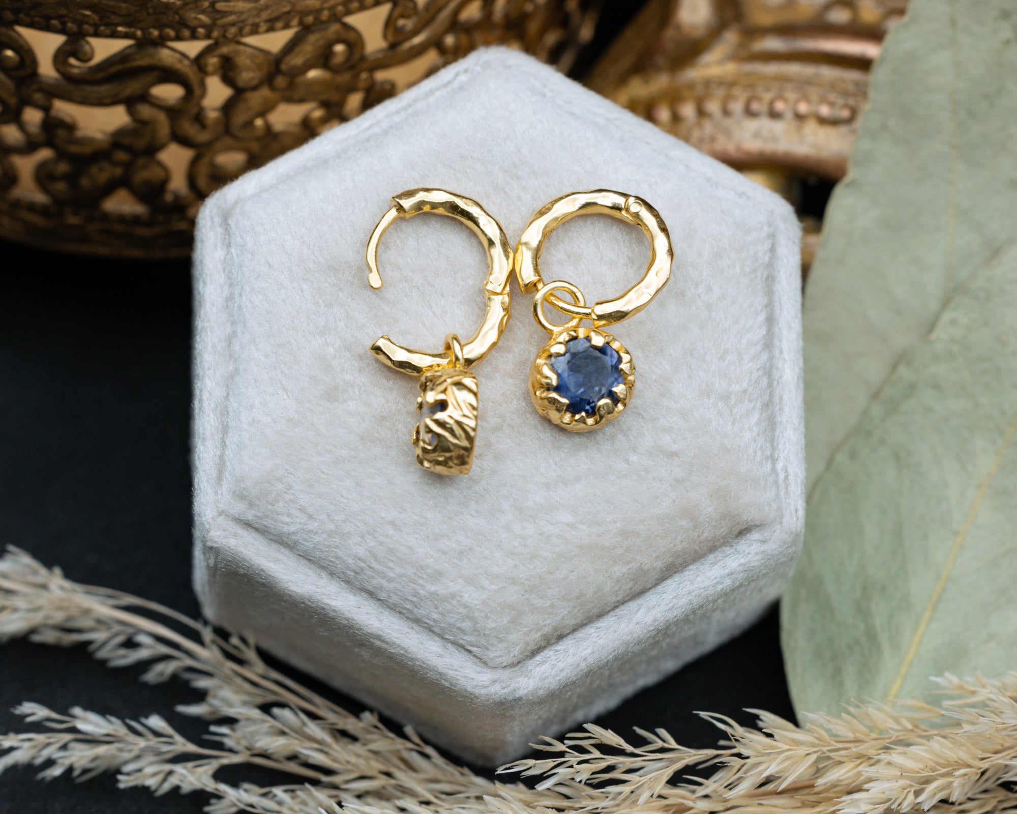 Gold hoop earrings with a blue sapphire on a white hexagonal jewelry box.