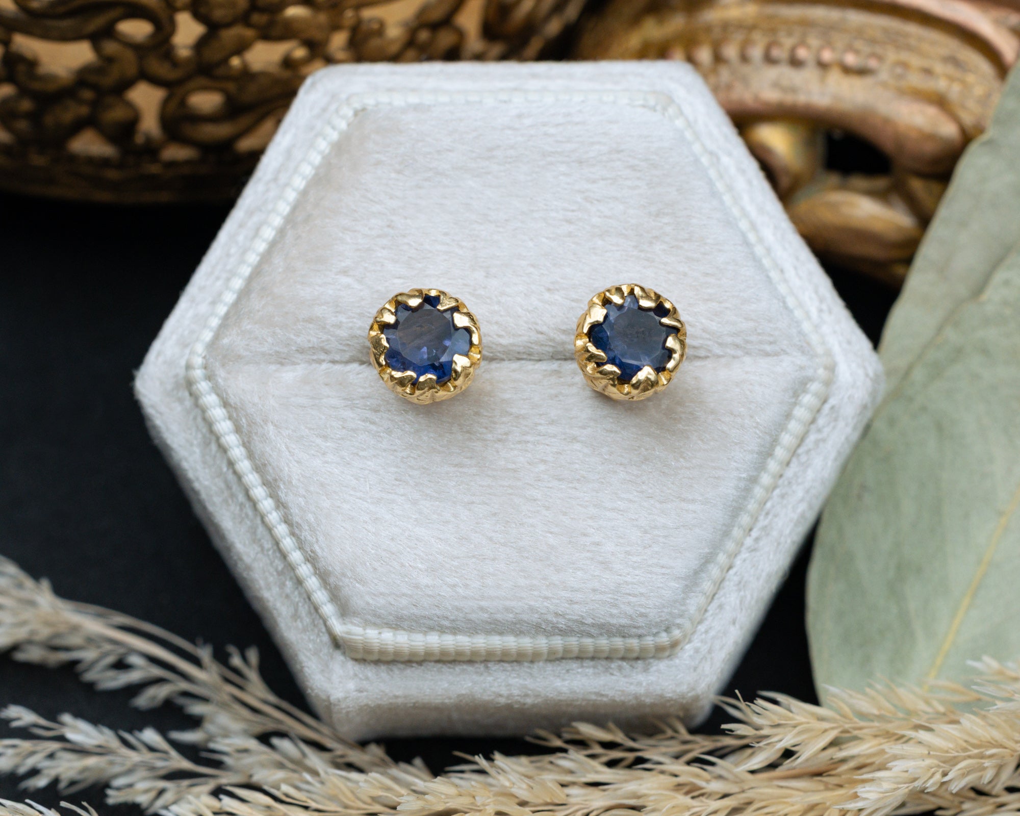 Gold earrings with blue sapphires on a white hexagonal jewelry box.