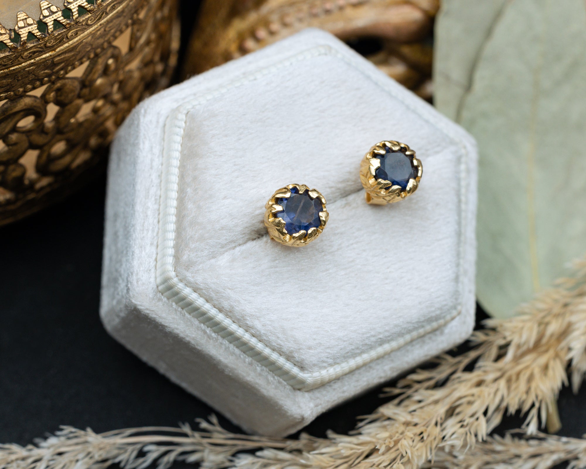 Gold earrings with blue sapphires on a white hexagonal jewelry box.