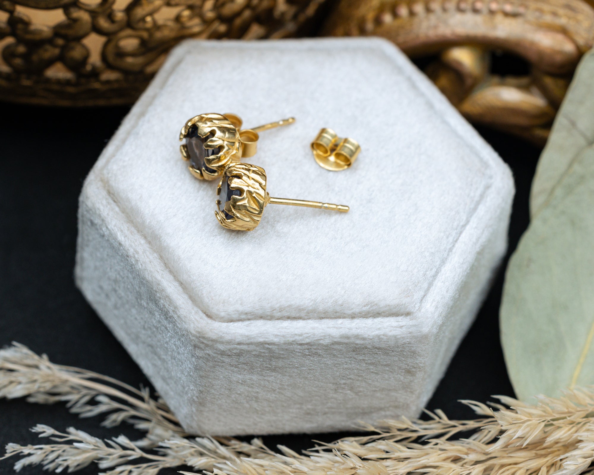 Gold sapphire earrings on a white hexagonal jewelry box with a textured background