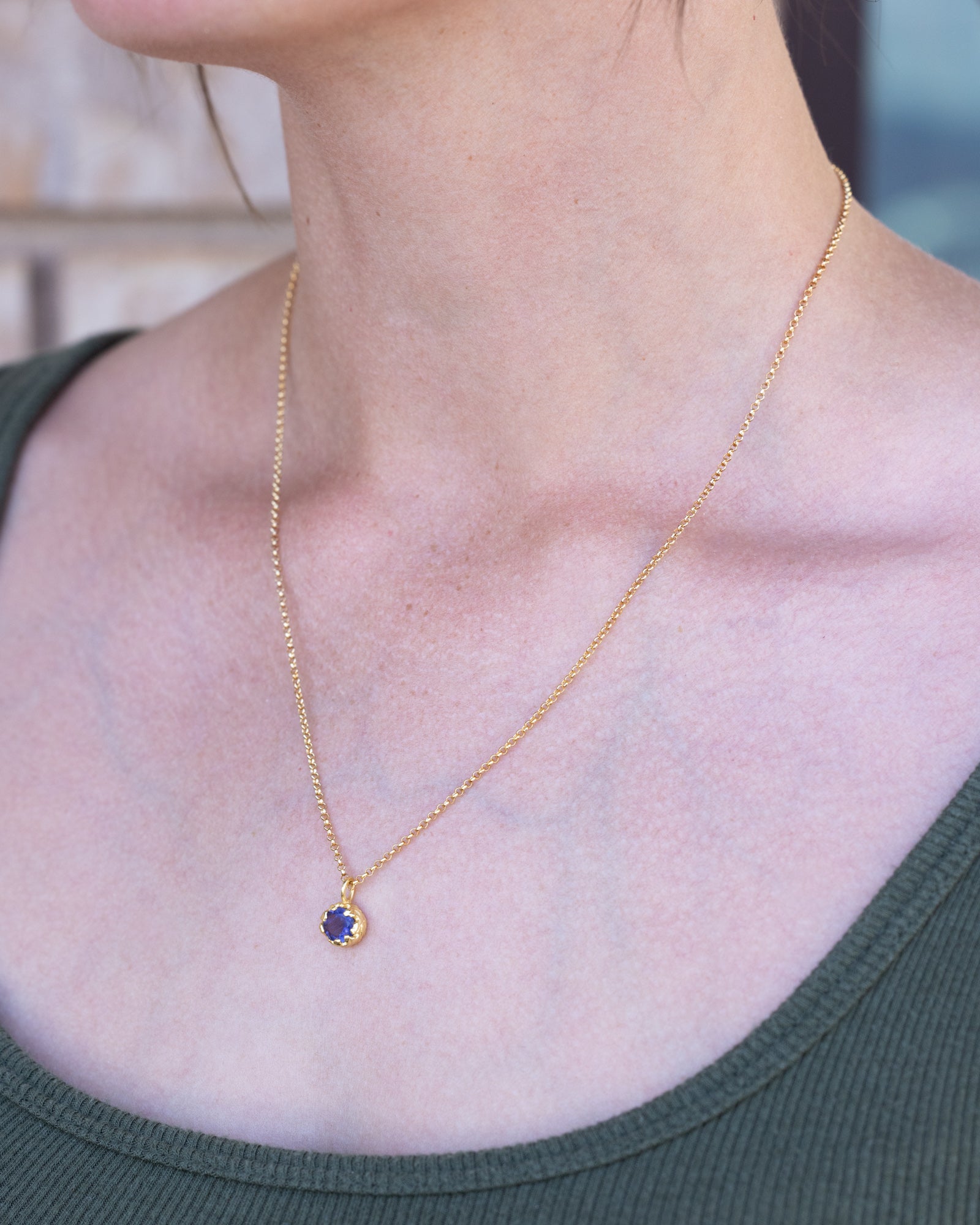 Gold necklace with a blue sapphire worn by a person in a green top.