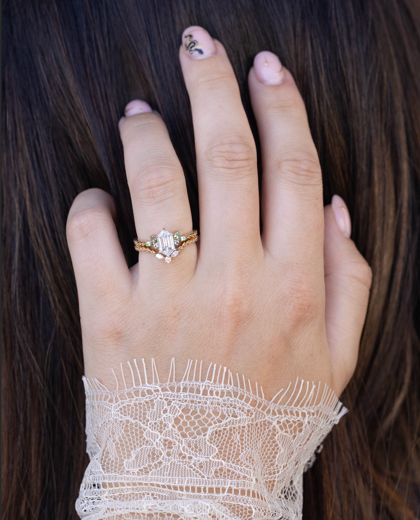 Hand wearing a diamond ring with lace sleeve against dark hair
