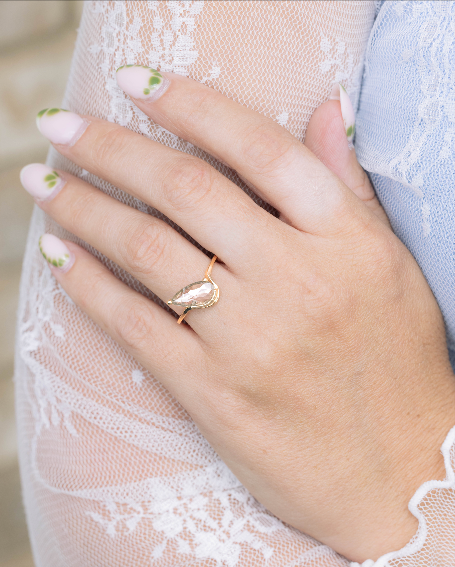 Hand wearing a gold ring with a decorative design, against a blurred background.