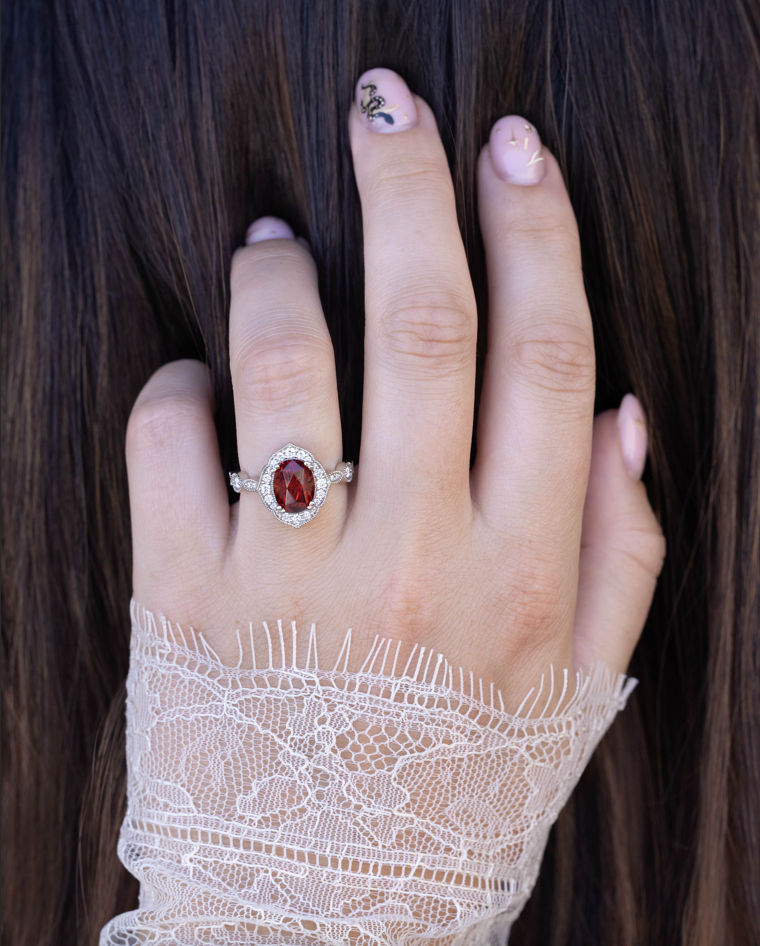 Hand wearing a white gold ring with a red garnet, held against dark hair.