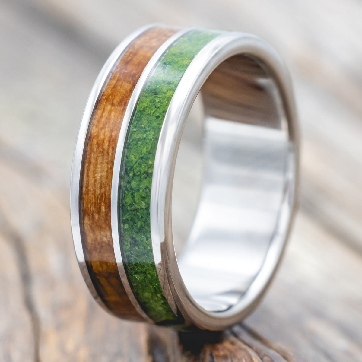 Titanium ring with whiskey barrel and moss inlay on a wooden surface