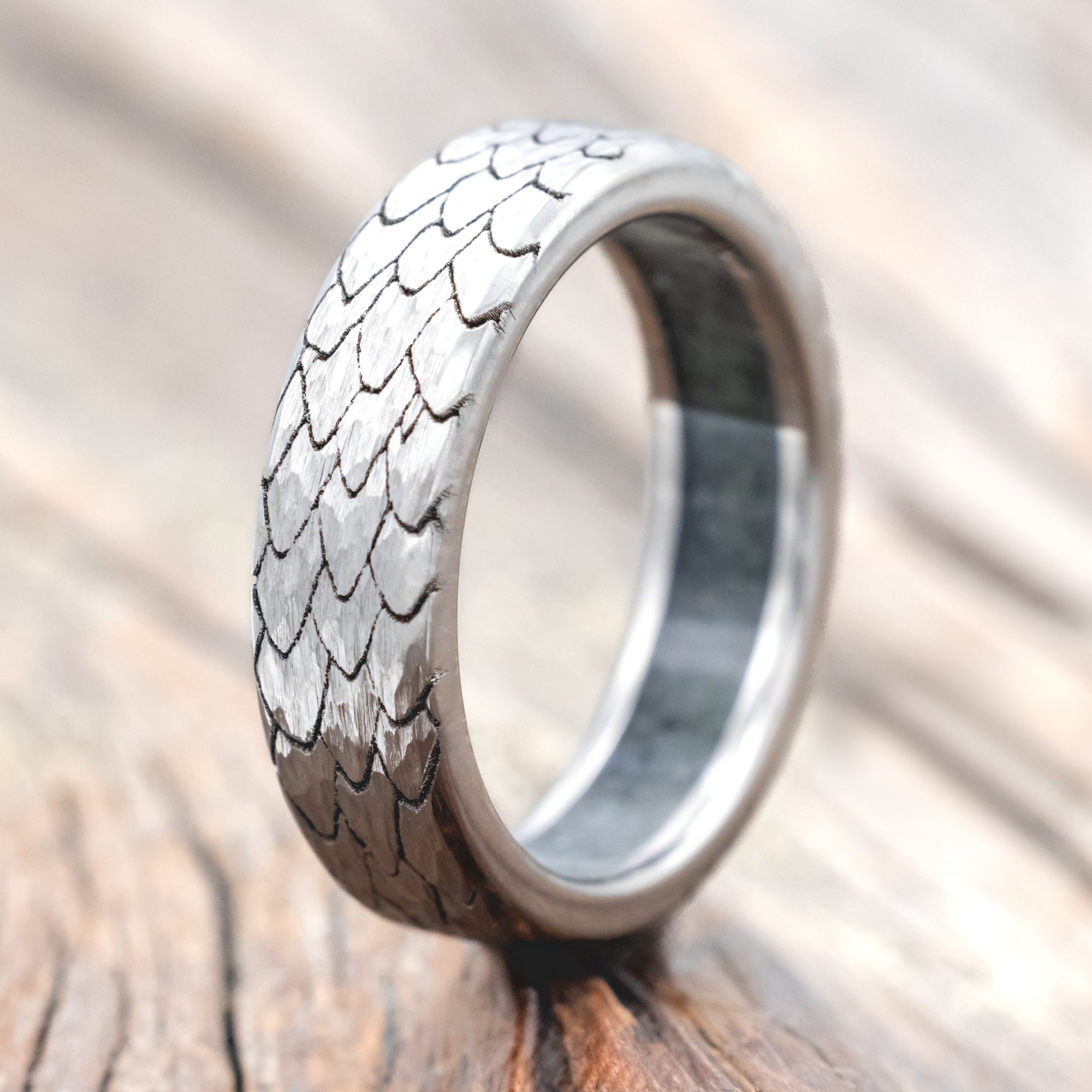 Titanium ring with textured dragon scale design on a wooden surface