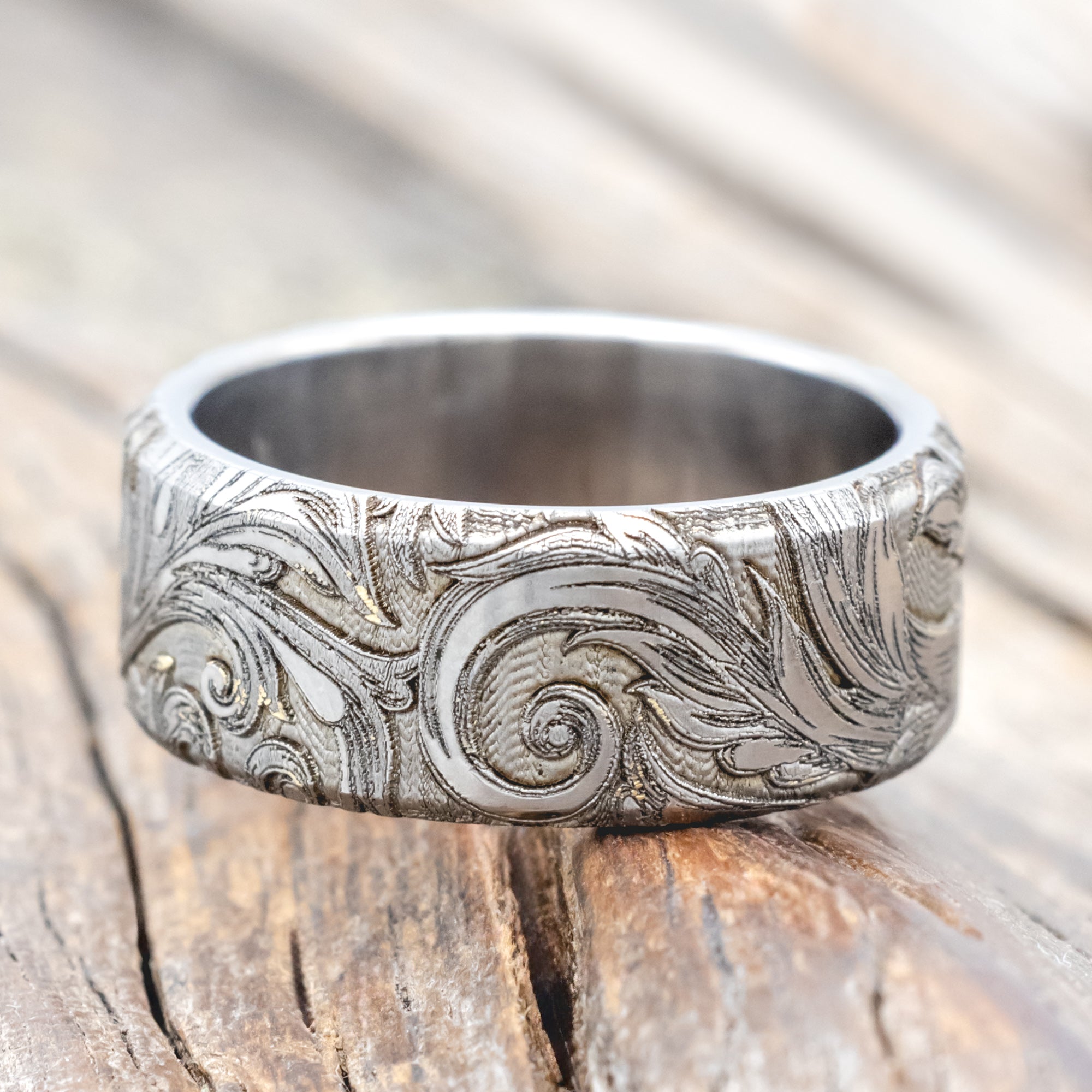 Titanium ring with intricate botanical engravings on a wooden surface
