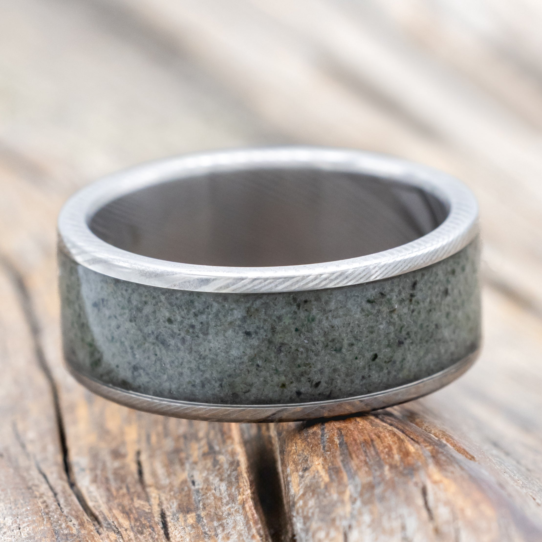 A Damascus steel ring with crushed moss agate inlay against a wooden background
