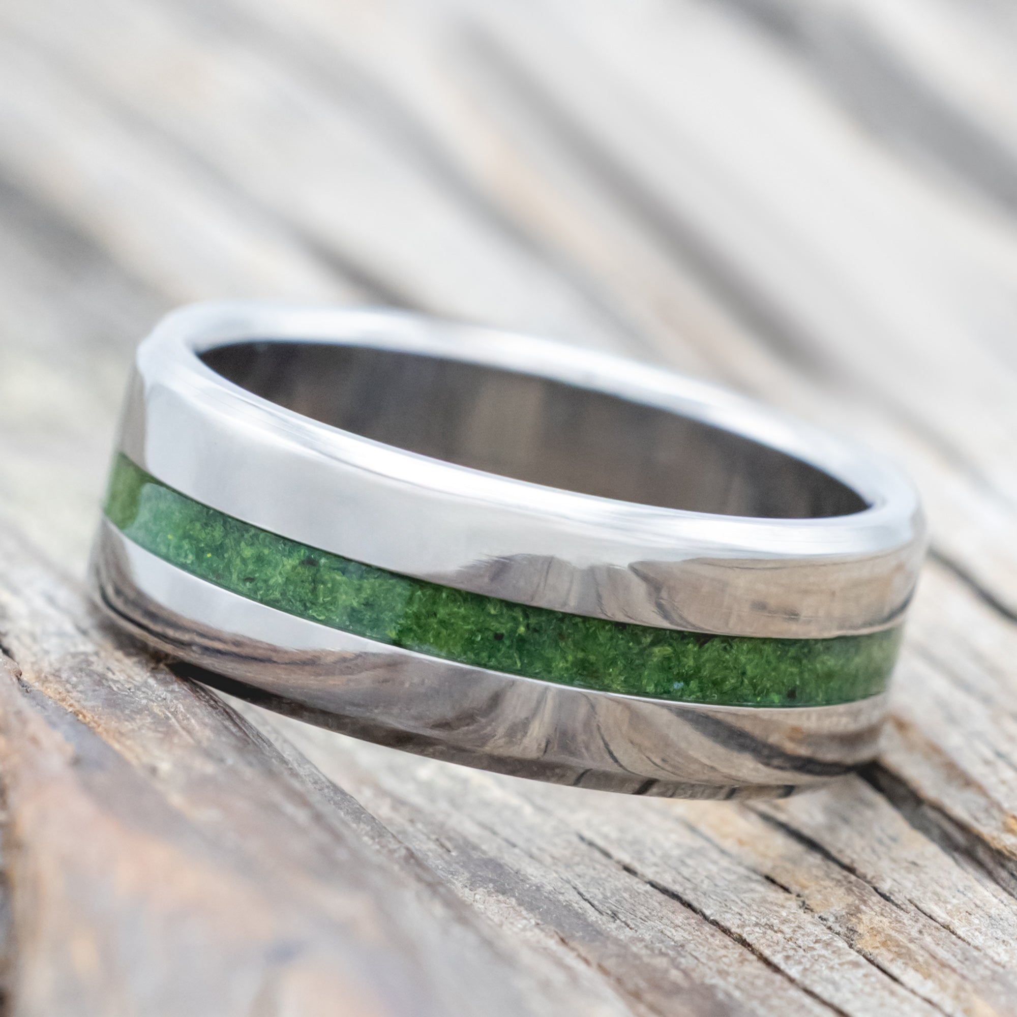 Titanium ring with moss inlay on a wooden surface