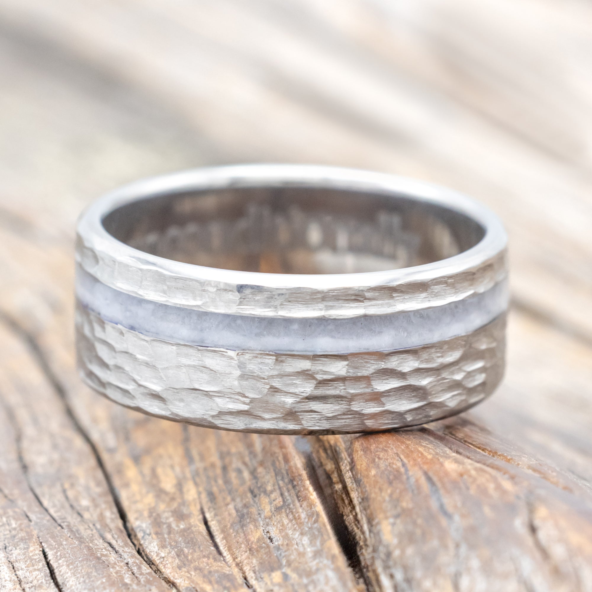 Hammered titanium wedding ring with wedding dress inlay on wooden surface