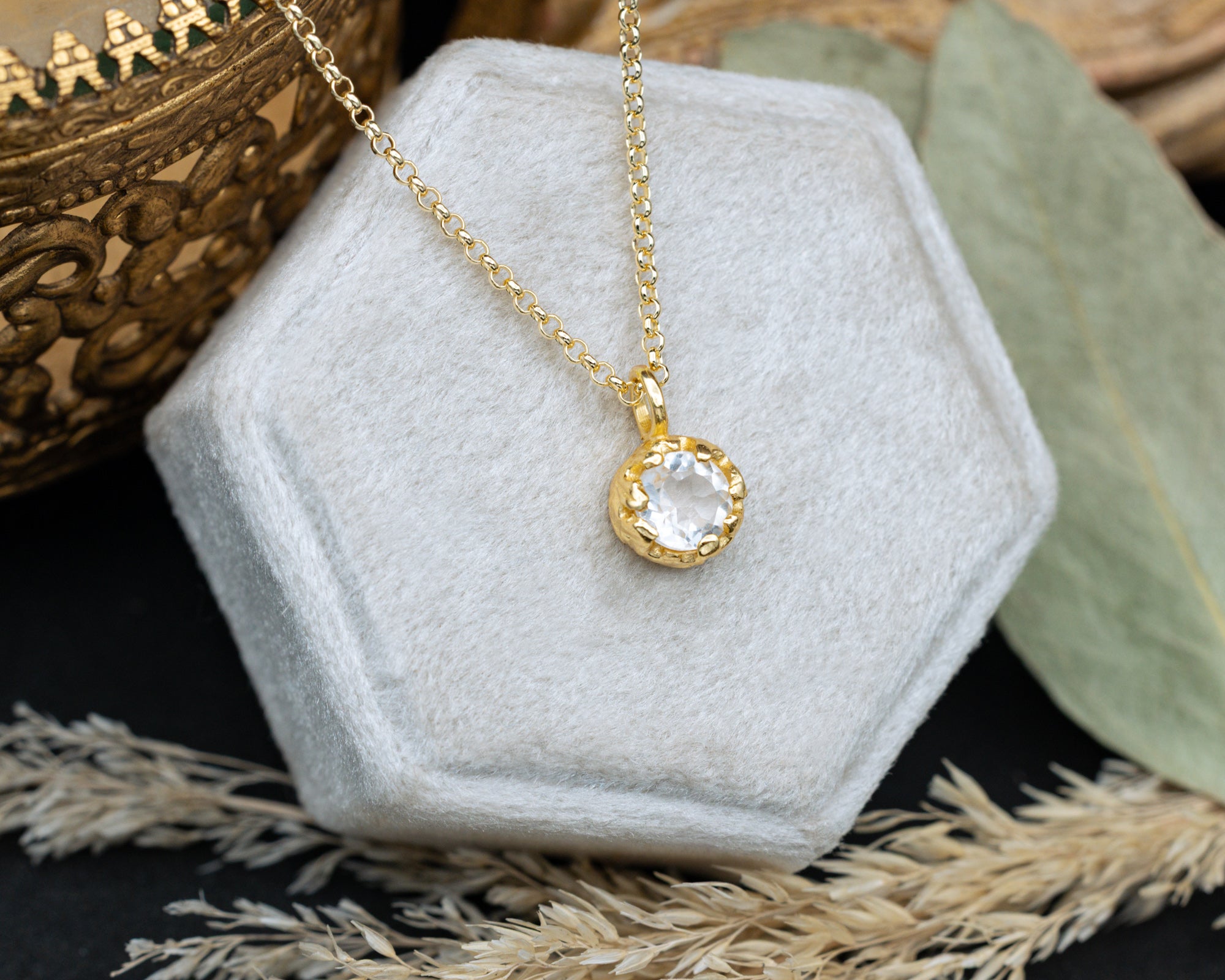 Gold necklace with a white topaz pendant on a hexagonal white stone