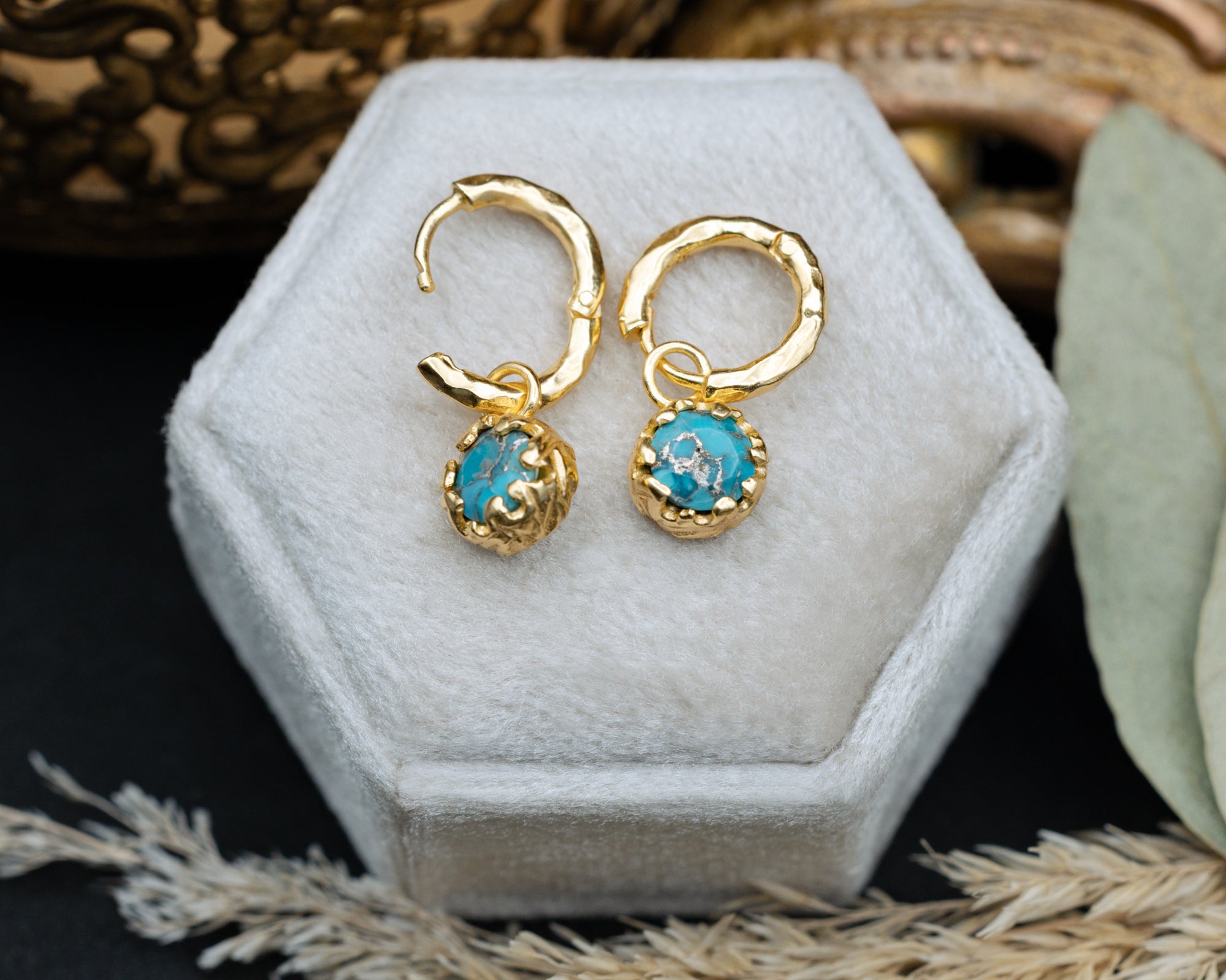 Gold hoop earrings with turquoise stones on a hexagonal jewelry box.