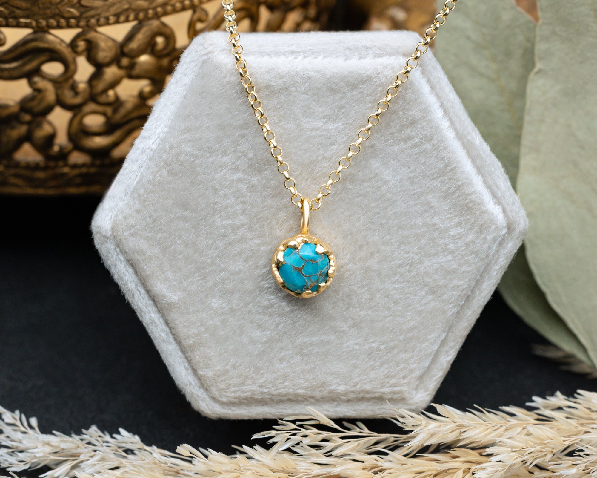 Gold necklace with a turquoise pendant on a hexagonal velvet stand.