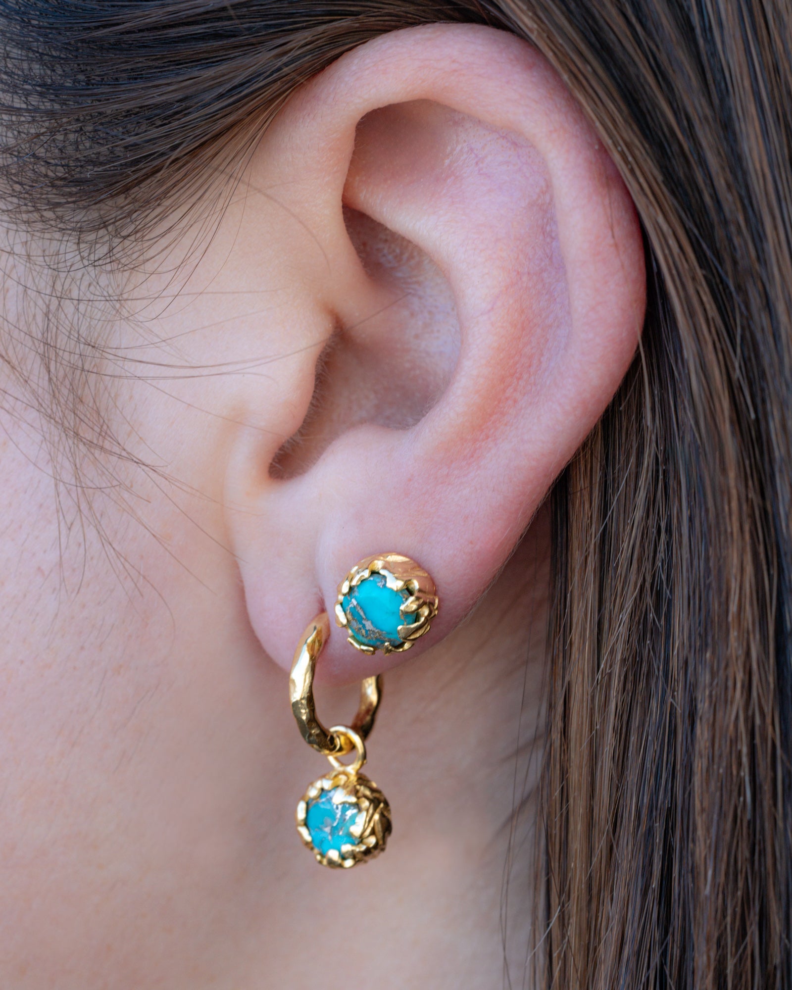 Gold earrings with turquoise stones worn by a person