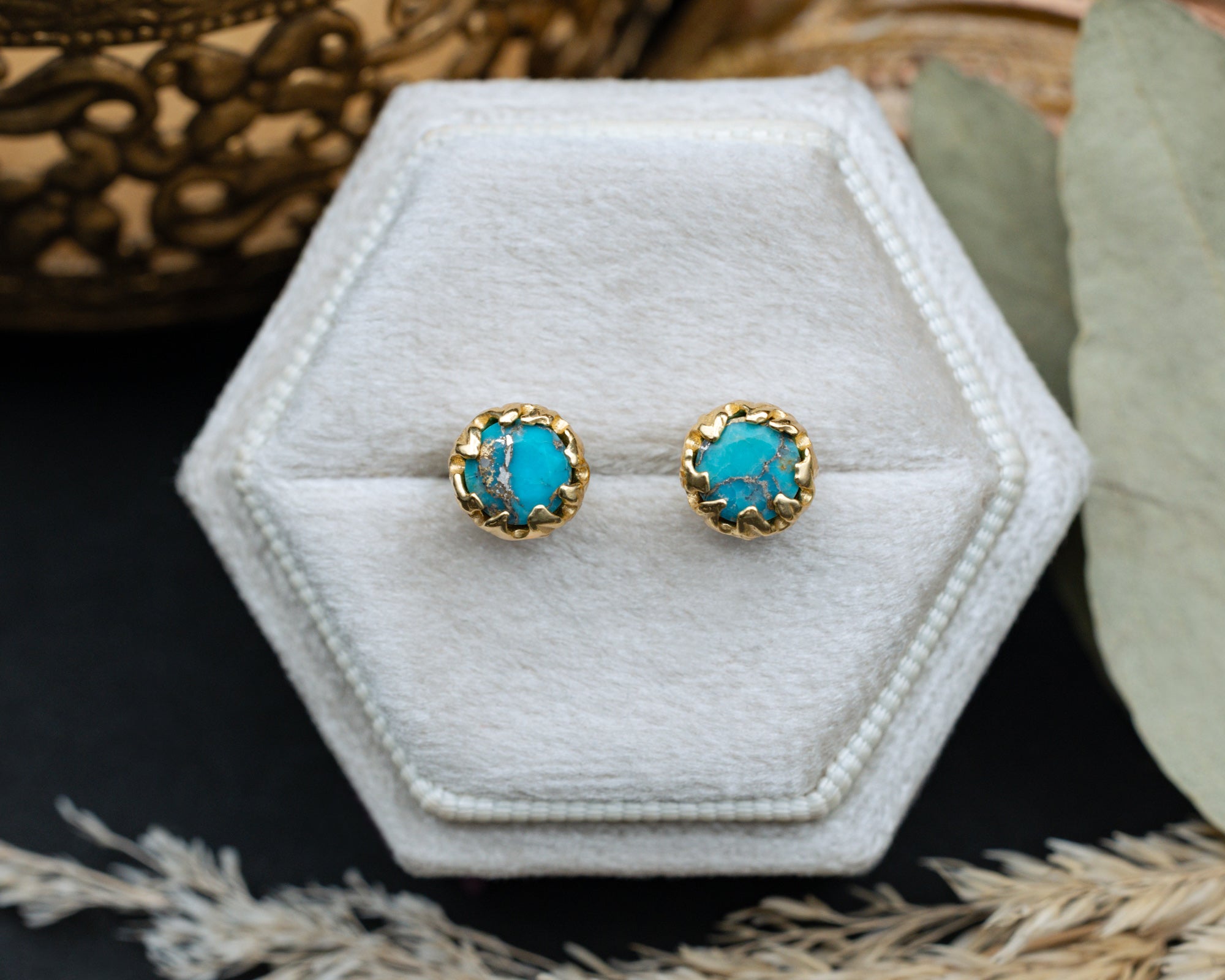 Turquoise earrings with gold accents on a white hexagonal stand.