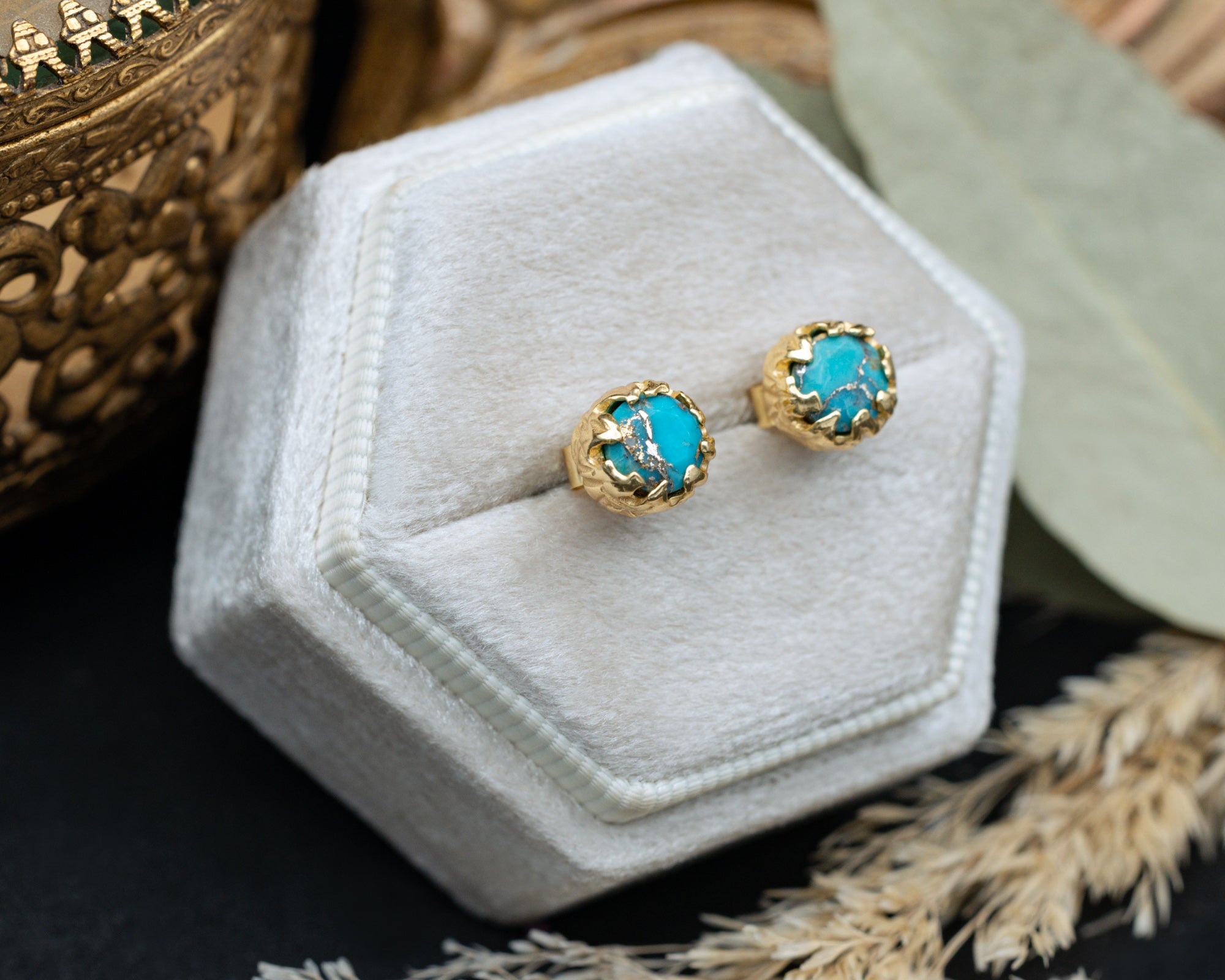 Gold earrings with turquoise stones on a white hexagonal jewelry display box.