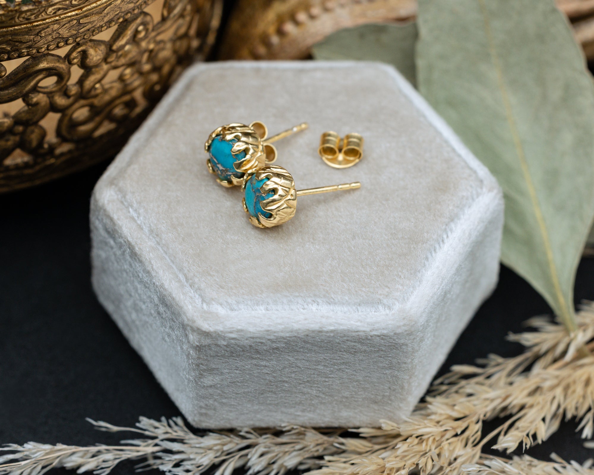 Gold earrings with turquoise stones on a hexagonal velvet box.