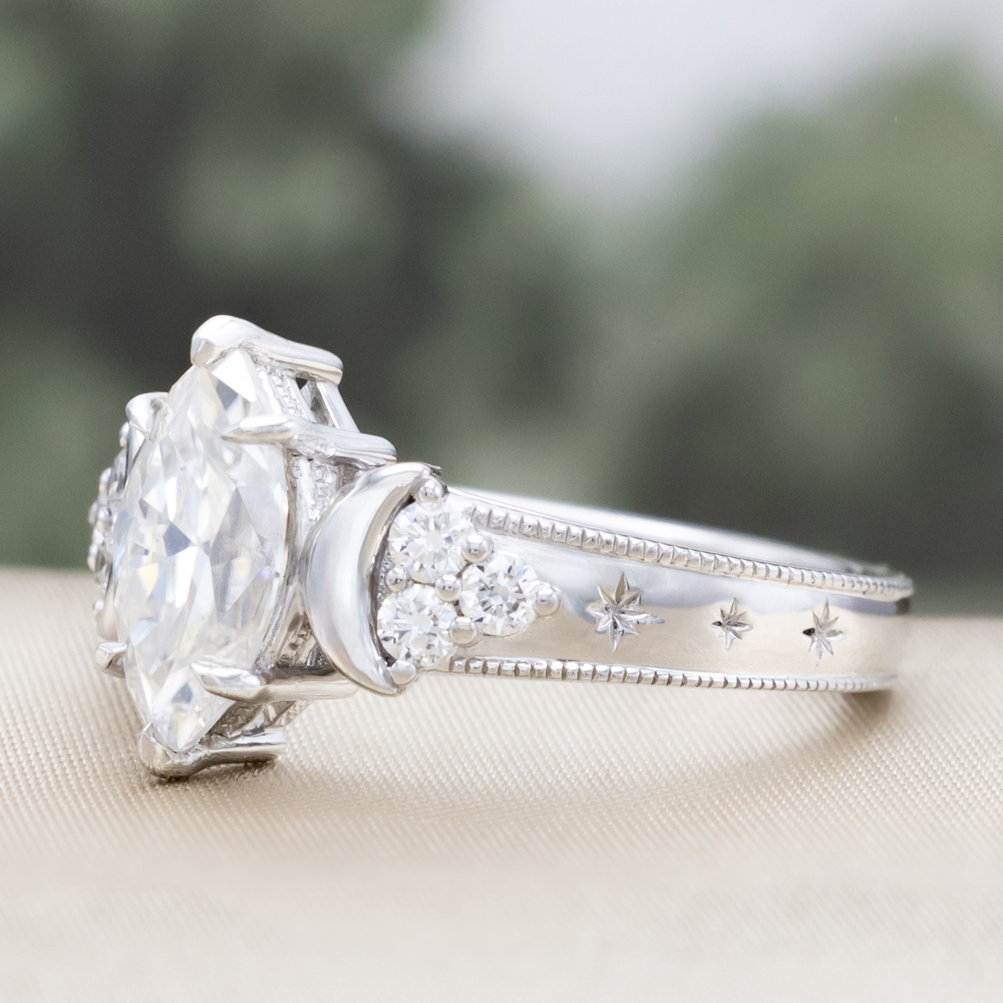 White gold ring with a large central moissanite and diamond accents on the band against a blurred green background
