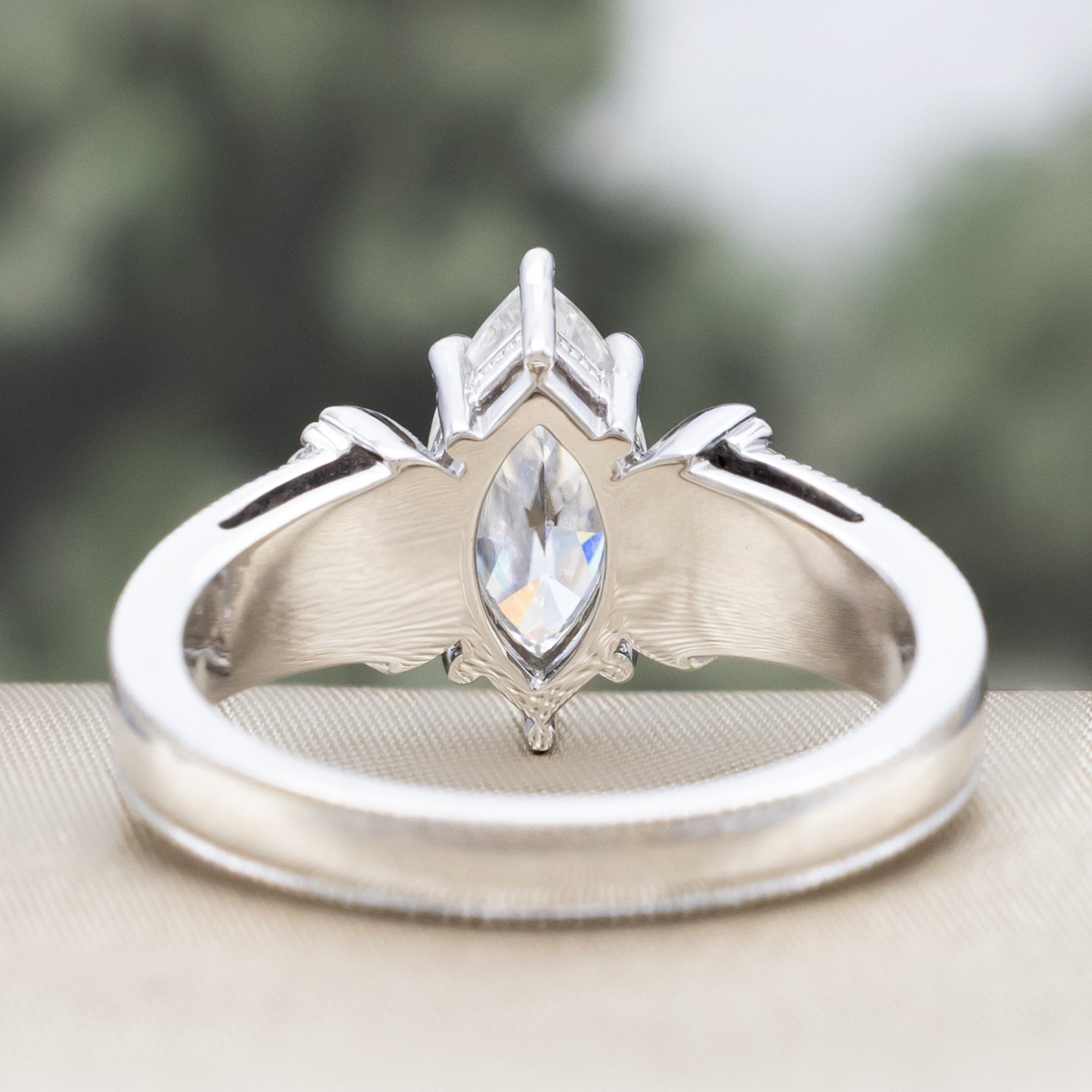 White gold ring with a large central moissanite and diamond accents on the band against a blurred green background