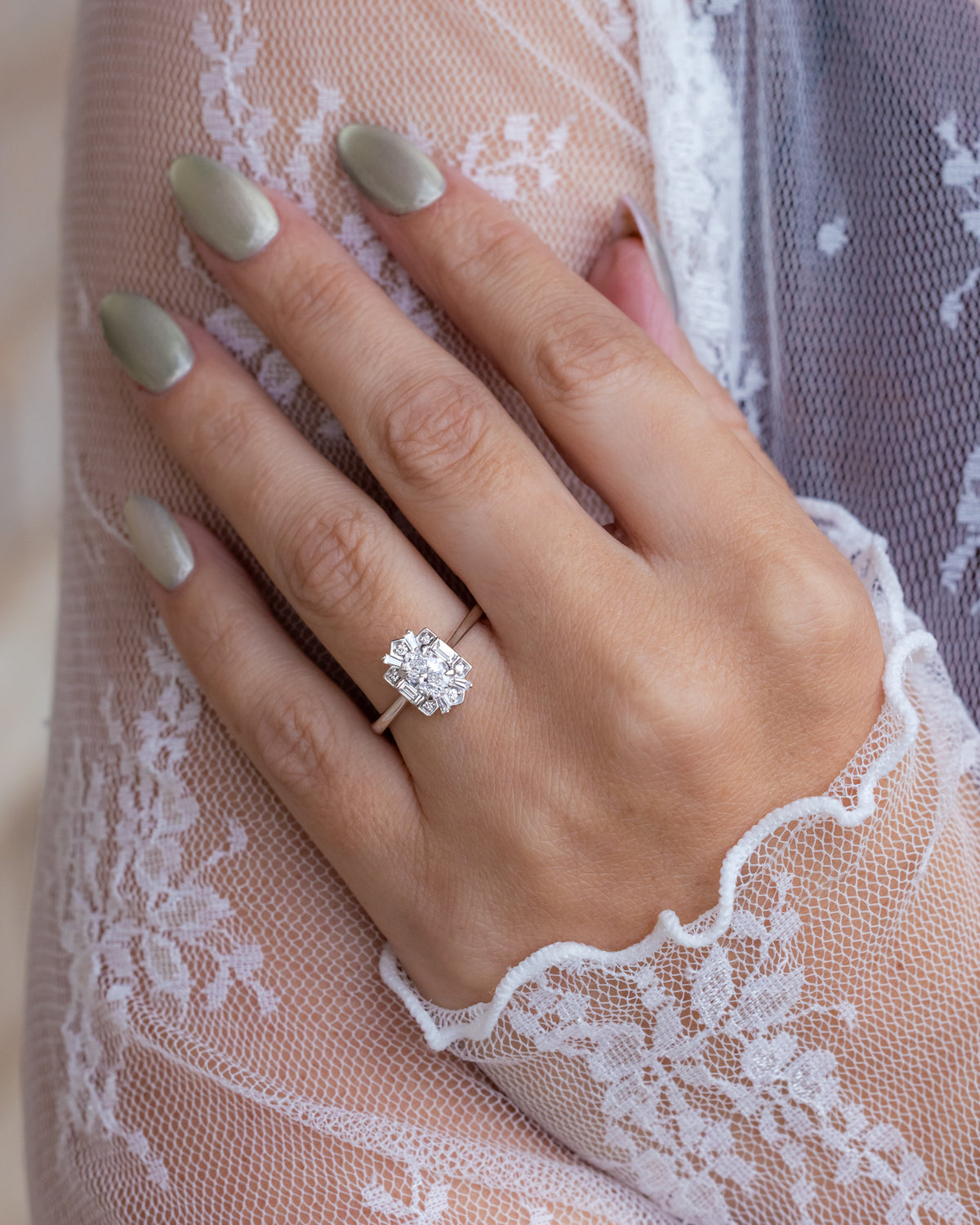 Hand wearing a diamond ring with lace fabric in the background
