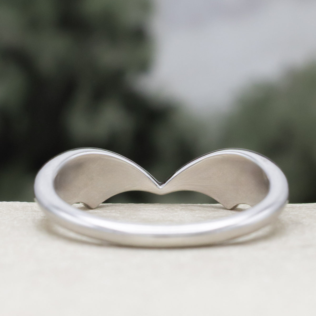 White gold bat wing wedding ring tracer against a blurred green background