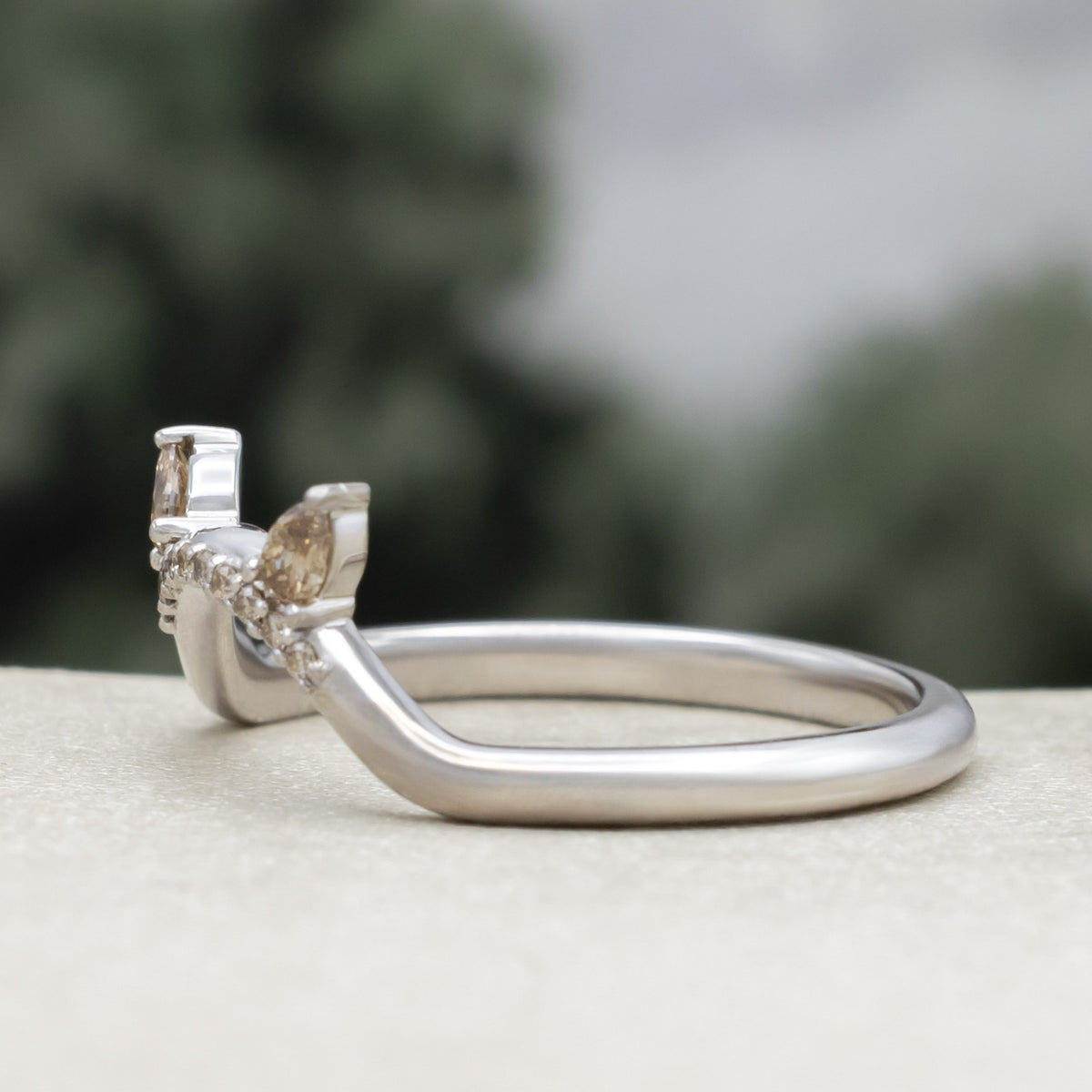 White gold cat ear wedding ring tracer with champagne diamond accents against a blurred green background