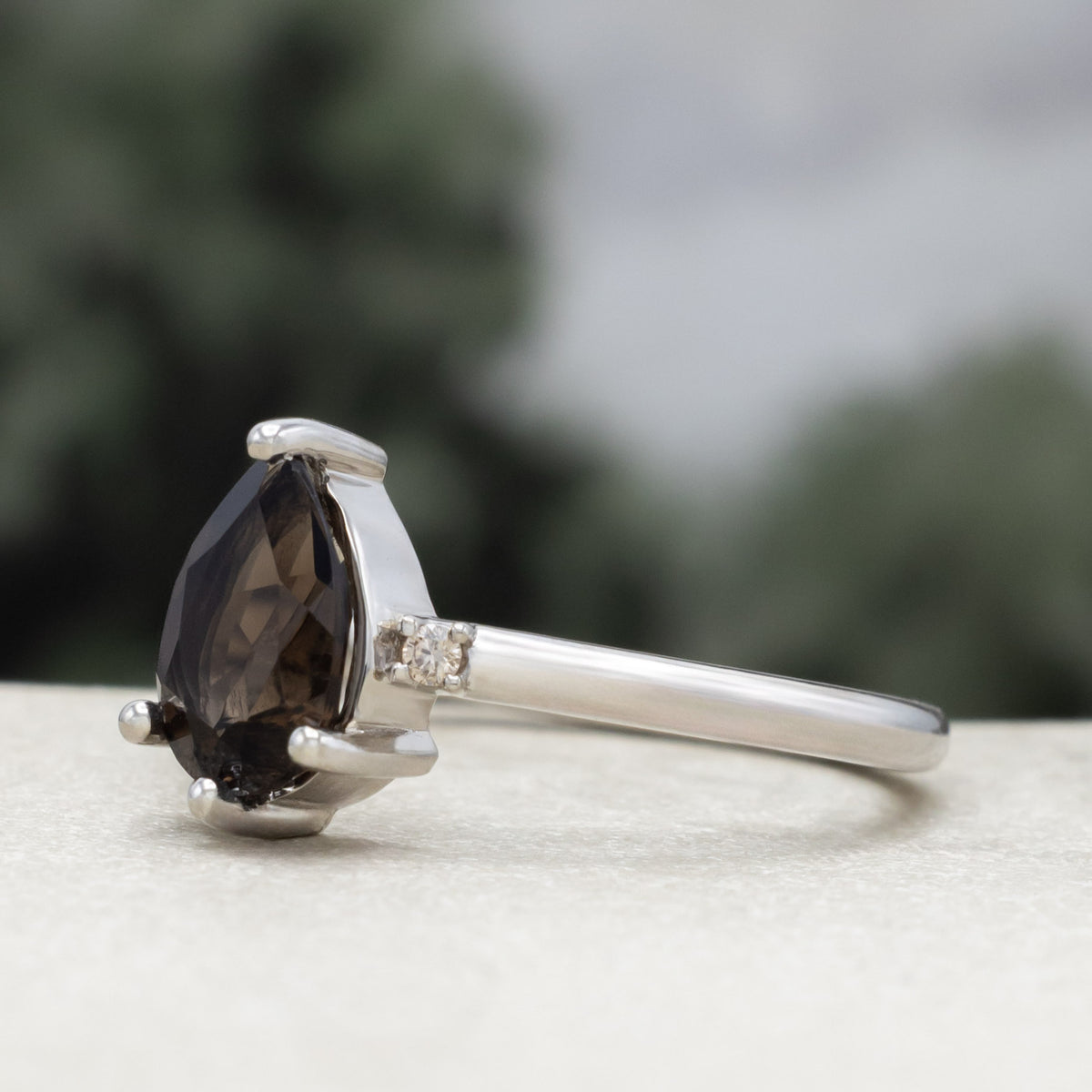 White gold engagement ring with smoky quartz center stone against a blurred green background