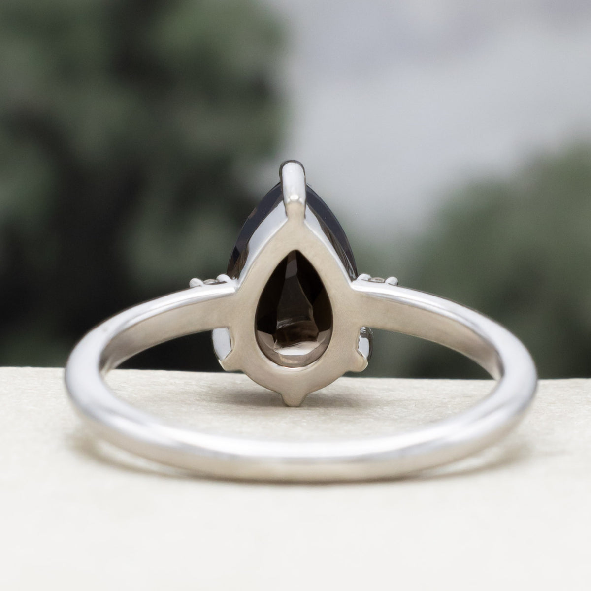 White gold engagement ring with smoky quartz center stone with champagne diamond accents against a blurred green background