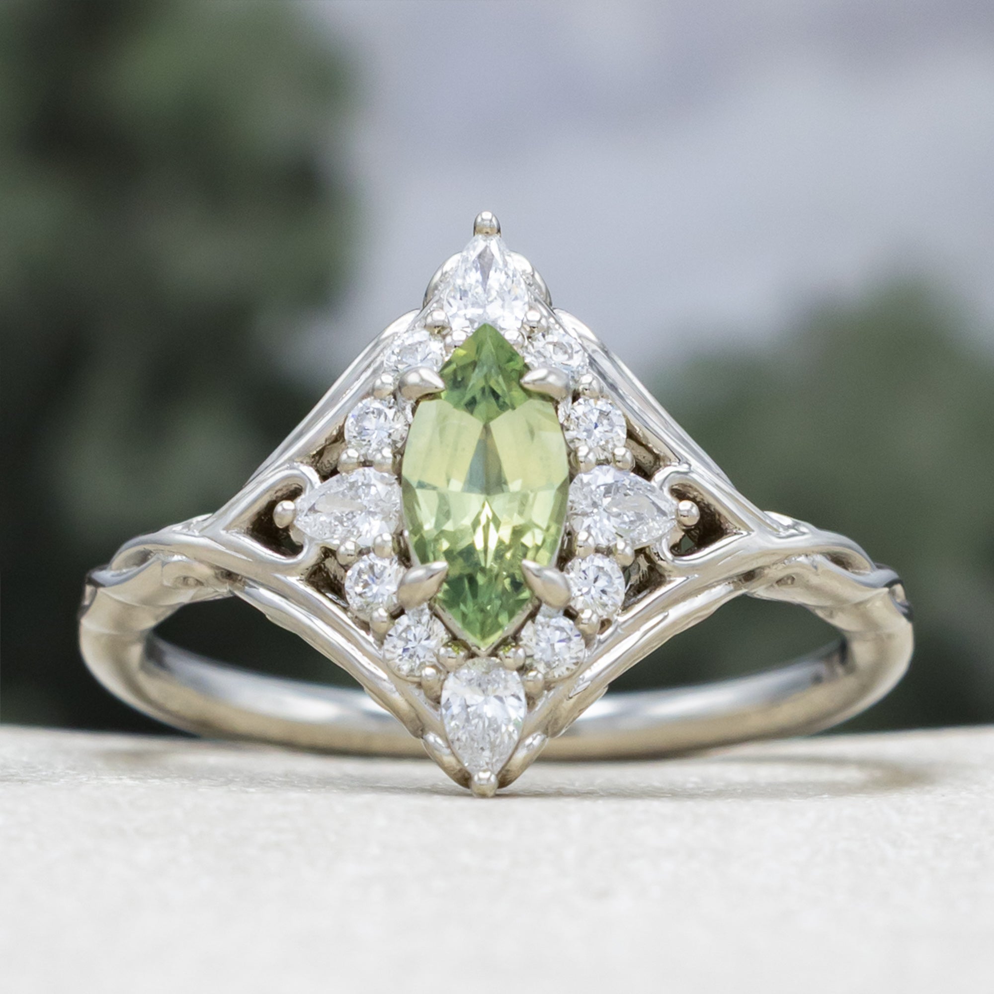 White gold ring with a green sapphire and diamond halo on a neutral background