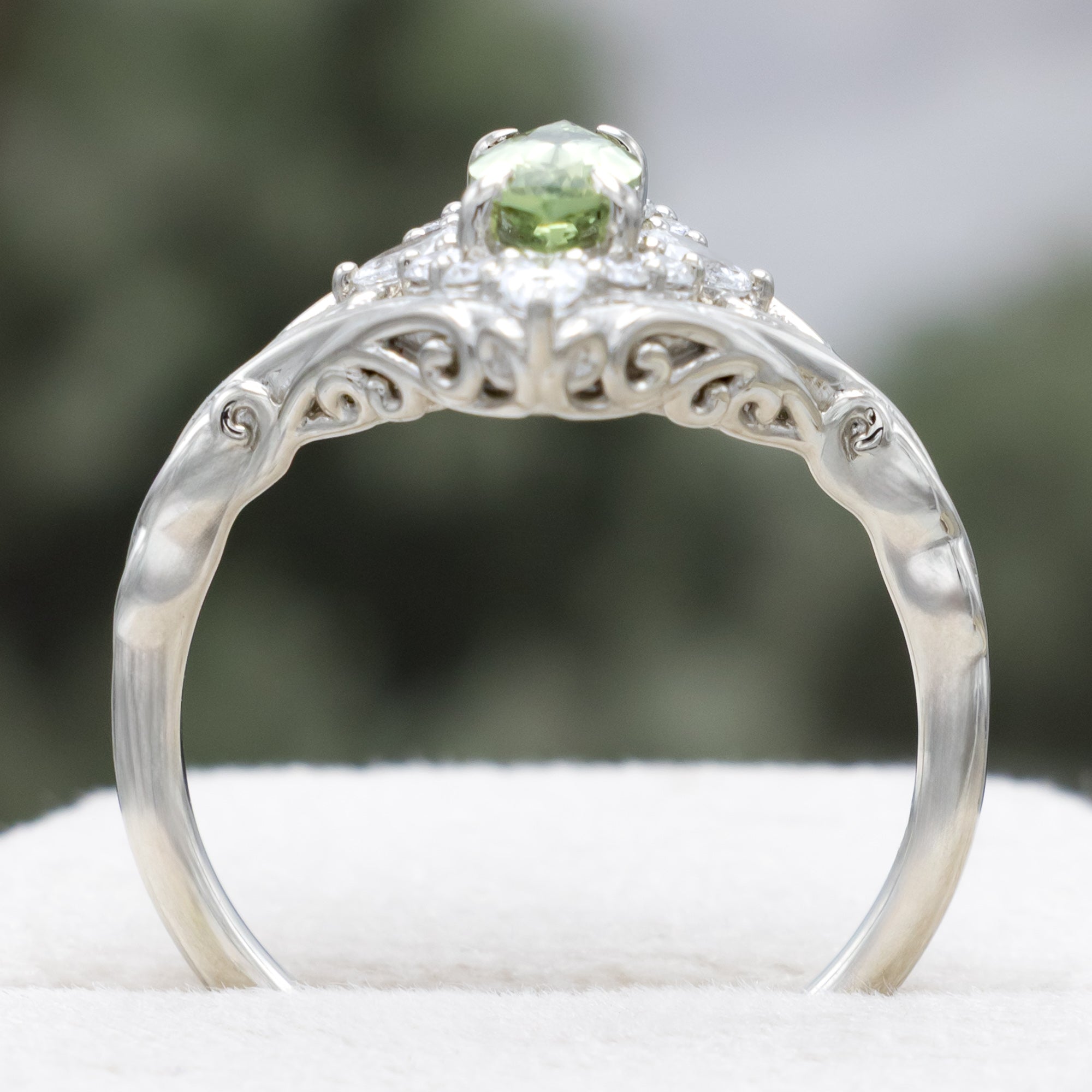 White gold ring with a green sapphire and diamond halo on a neutral background