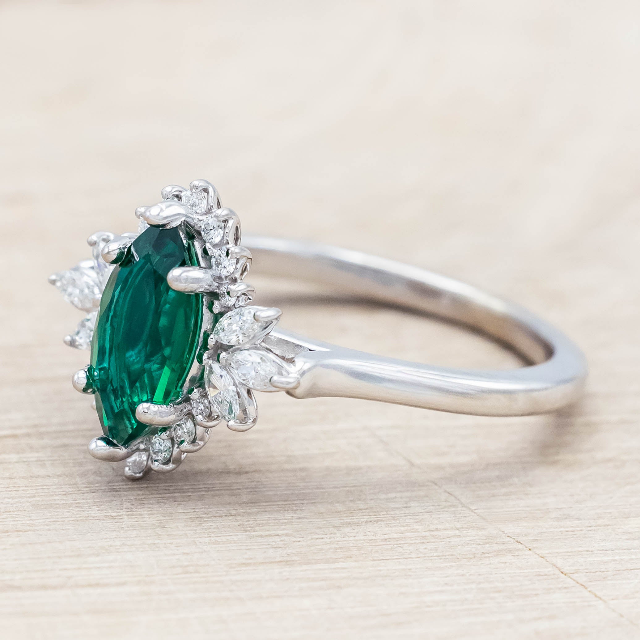 14K white gold ring with a green emerald on a light wooden background