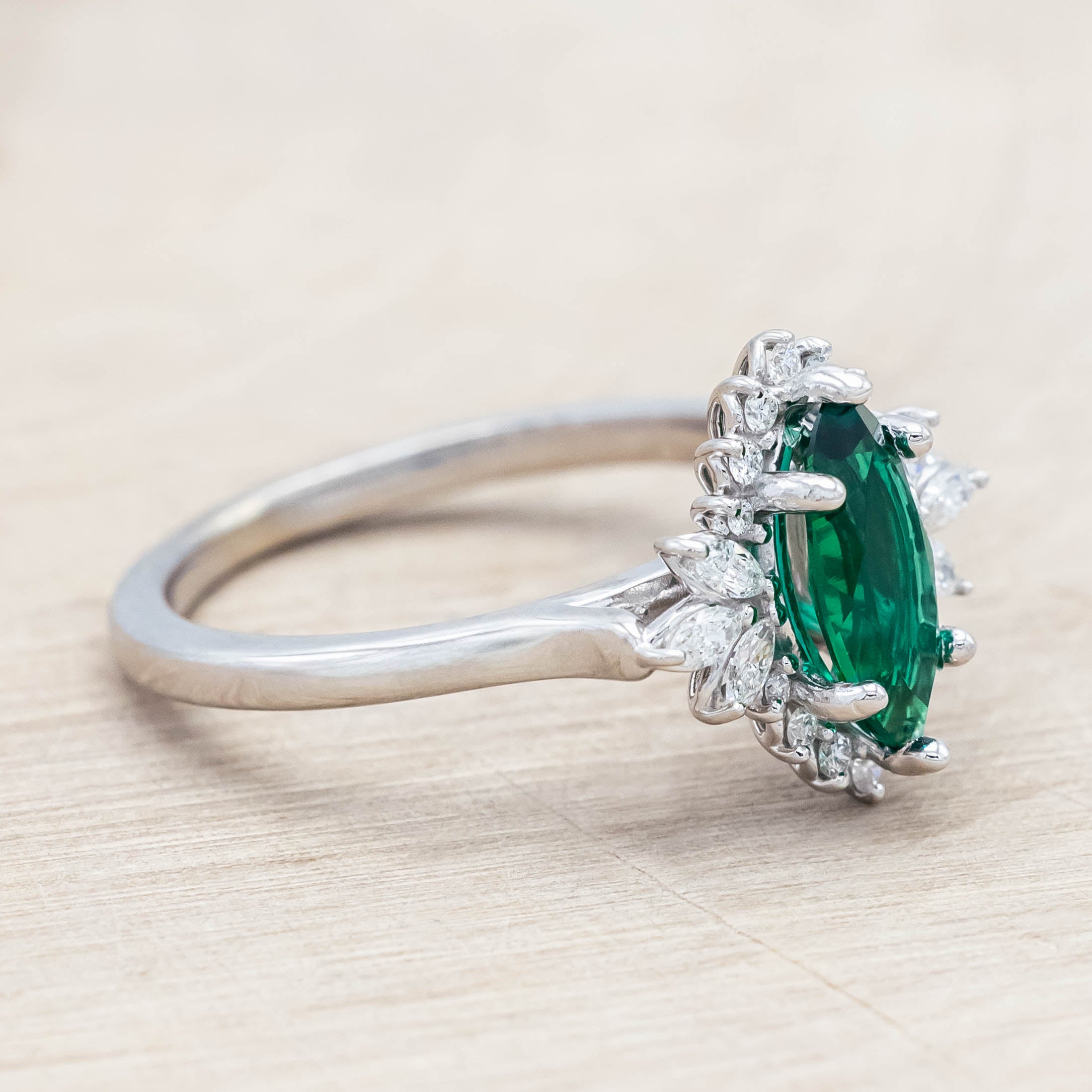 14K white gold ring with a green emerald on a light wooden background