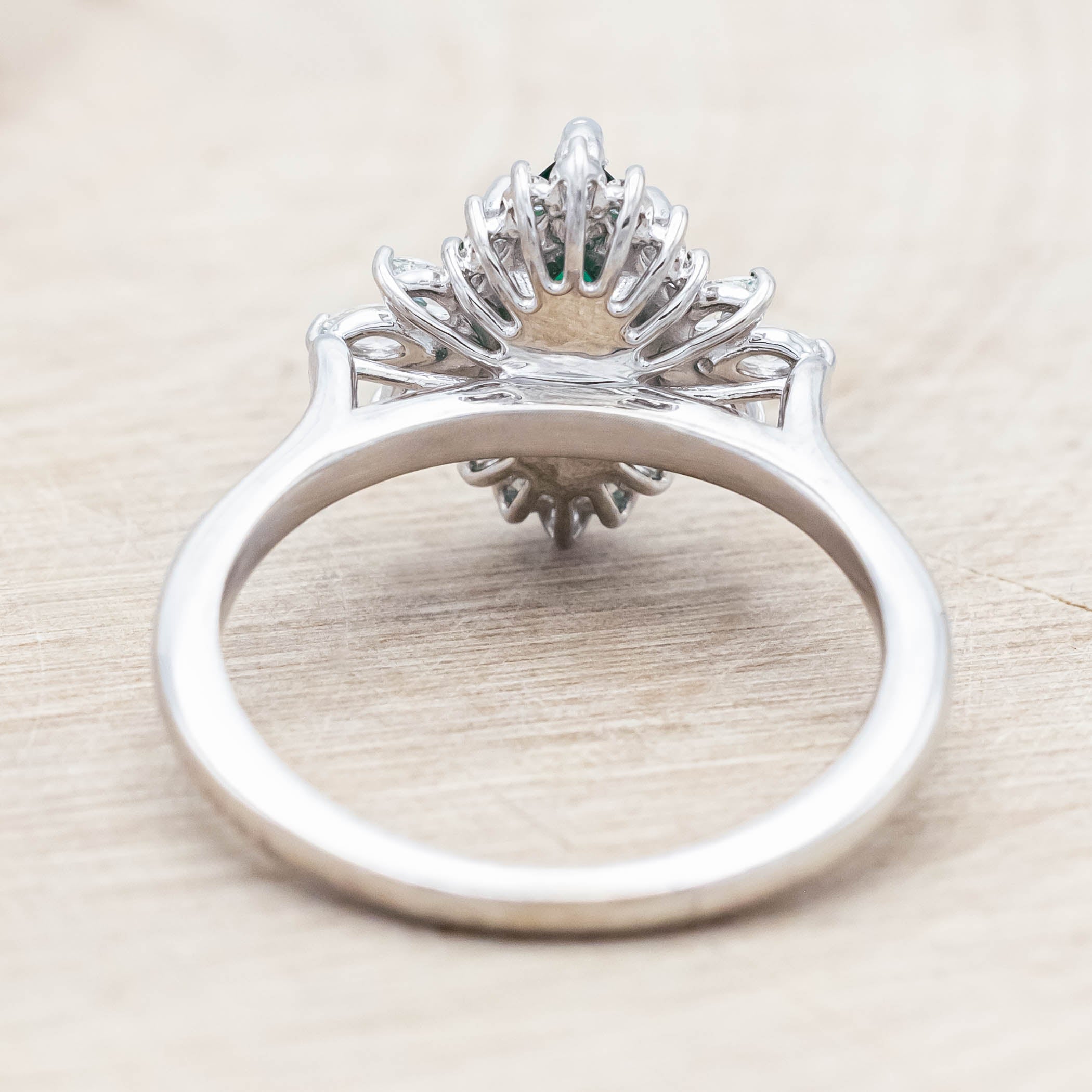 14K white gold ring with a green emerald on a light wooden background