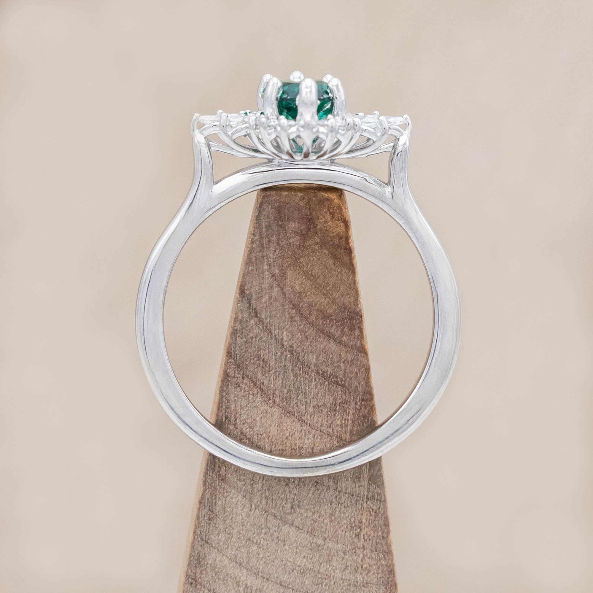 14K white gold ring with a green emerald on a wooden stand against a beige background