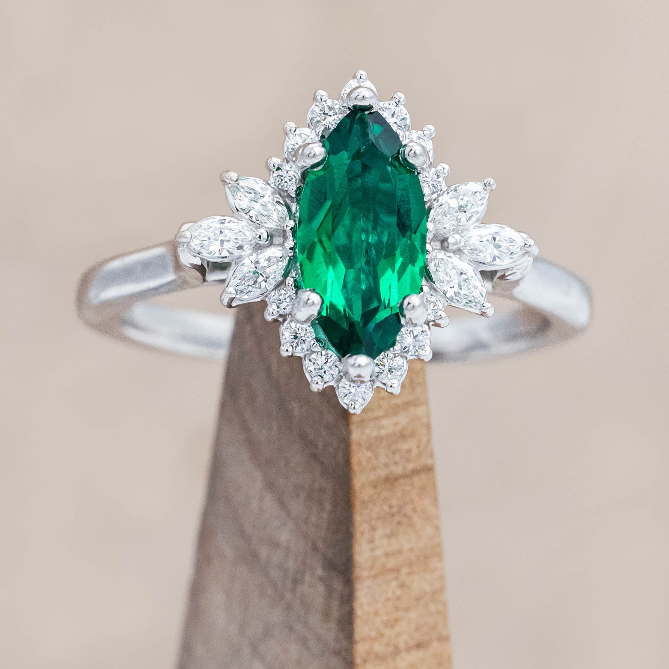 14K white gold ring with a green emerald on a wooden stand against a beige background