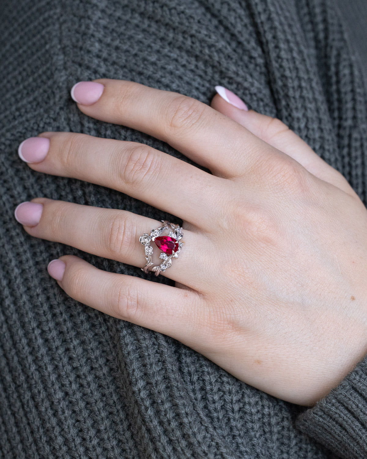 On hand "Harlow" pear cut ruby engagement ring with salt & pepper diamond accents on a branch-inspired band and floral style tracer