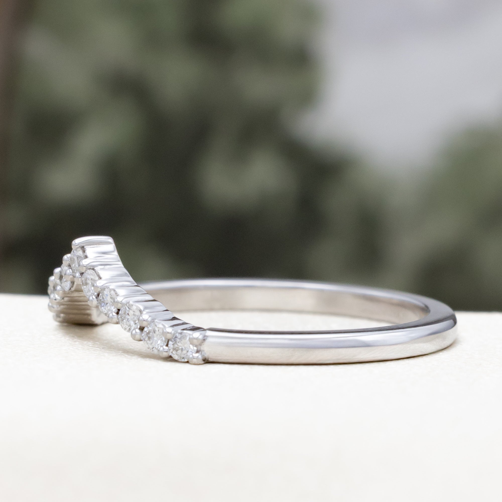 White gold ring with diamond accents on a blurred natural background