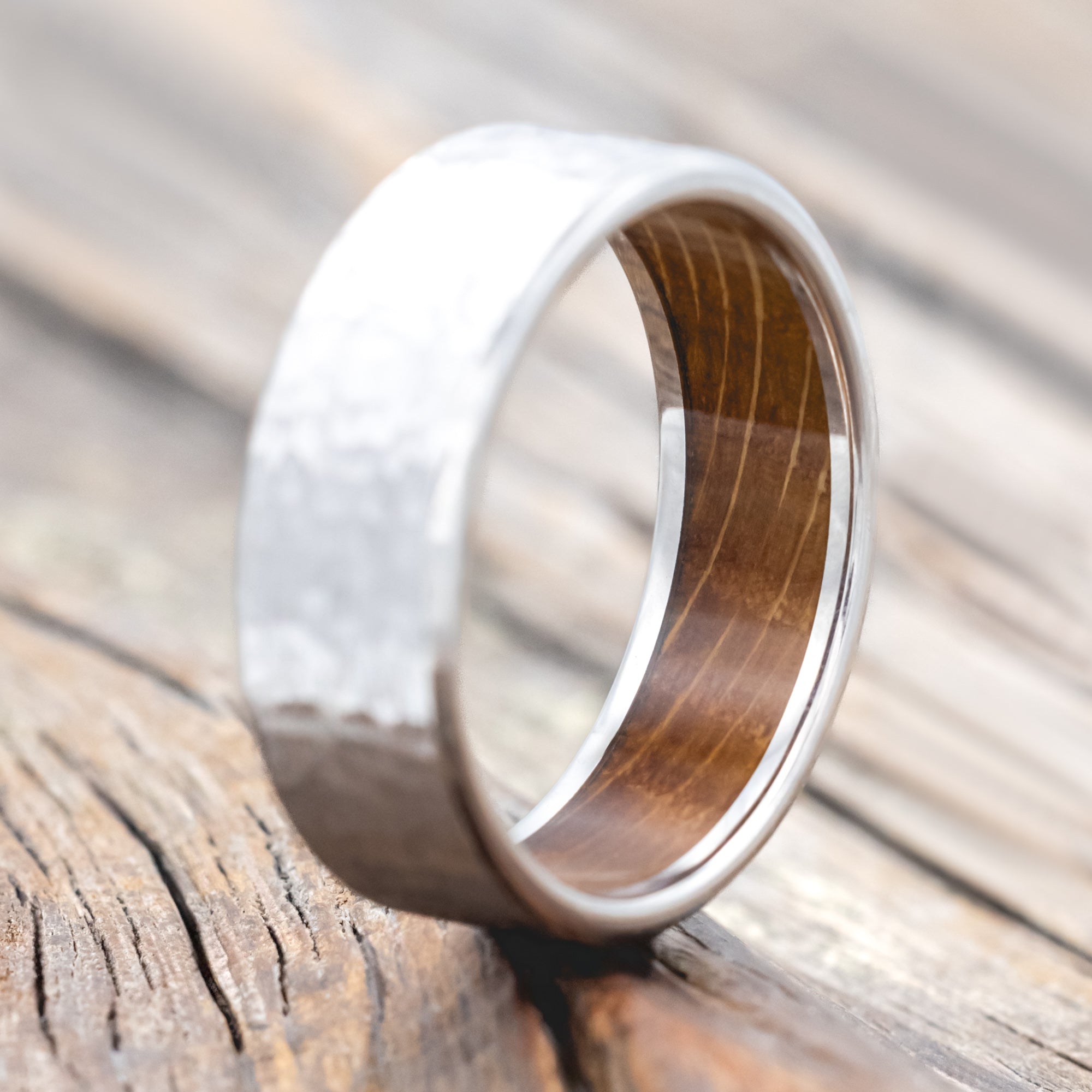 Hammered white gold ring with whiskey barrel oak lining on a wooden surface