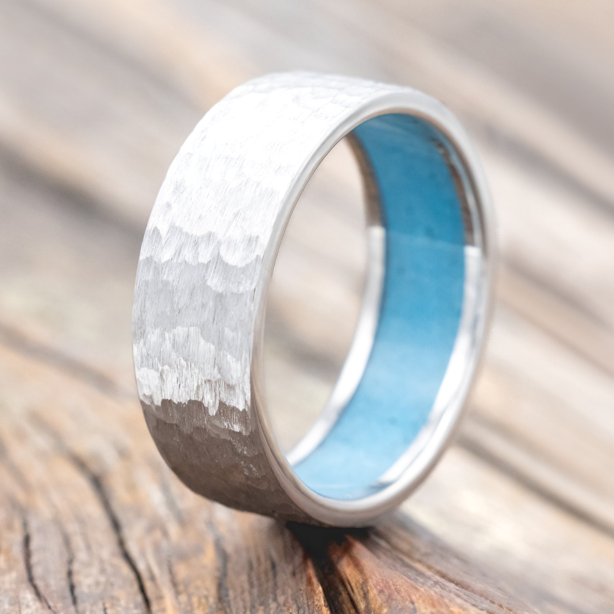 Hammered white gold ring with turquoise lining on a wooden surface