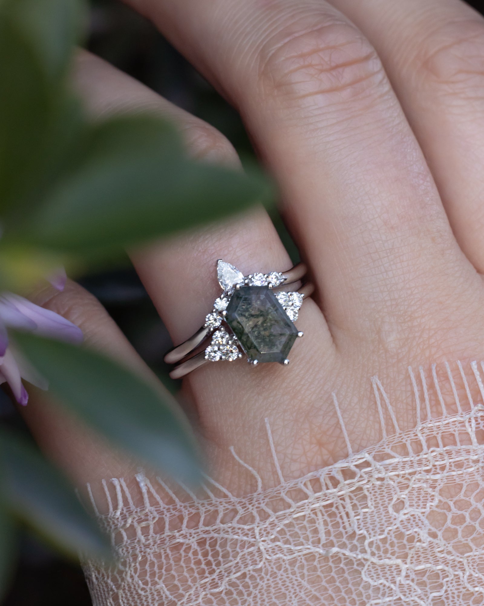 Close-up of a hand wearing a ring and tracer with moss agate, against a blurred natural background.