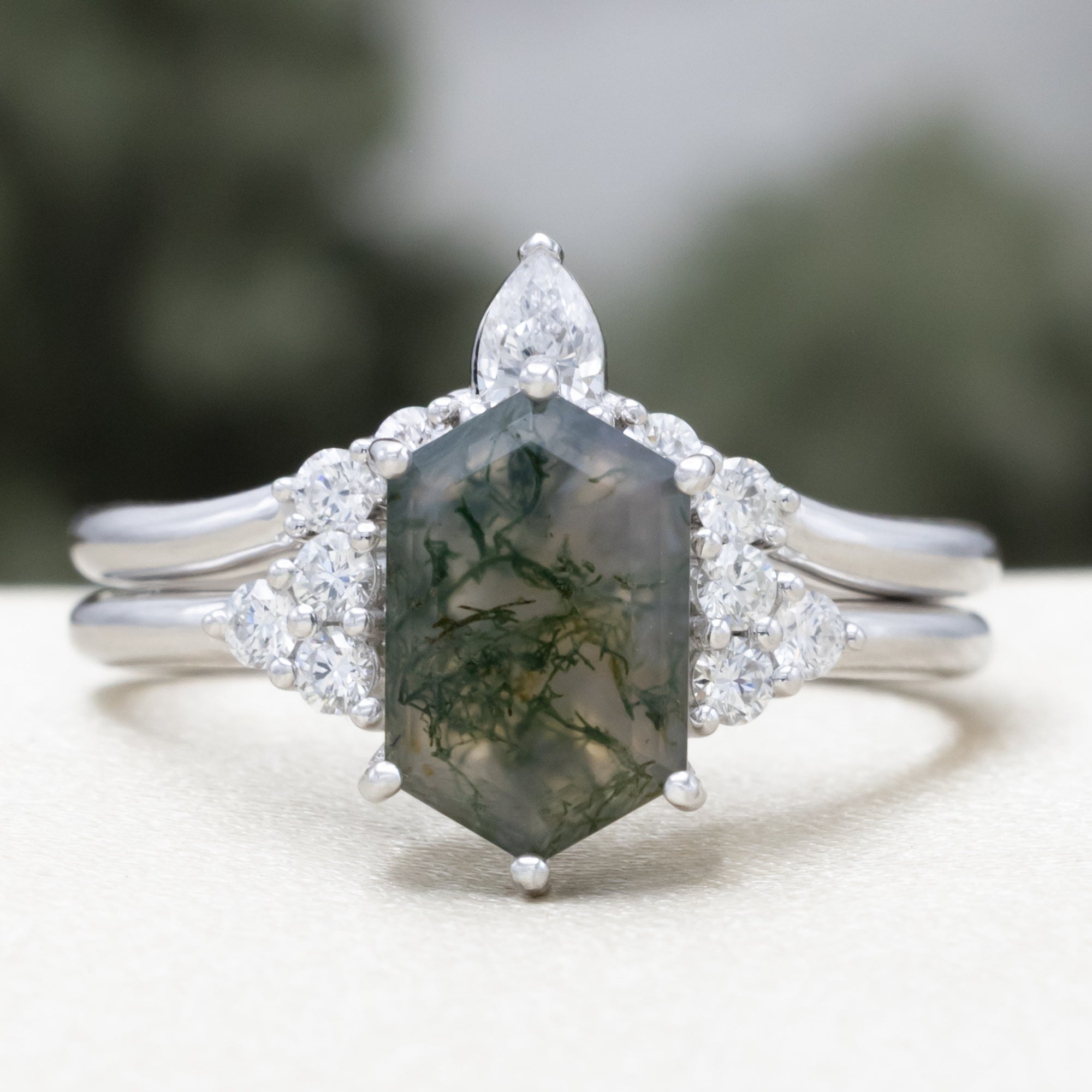 14K white gold engagement ring and tracer with moss agate and diamond accents on a blurred background