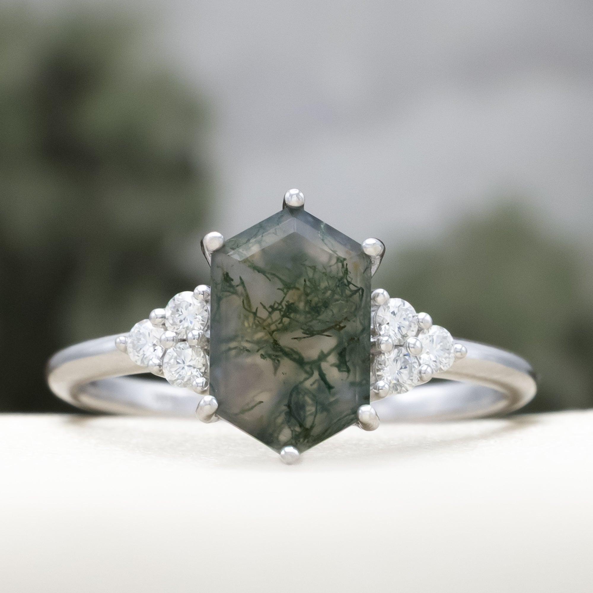 14K white gold engagement ring with moss agate on a blurred background