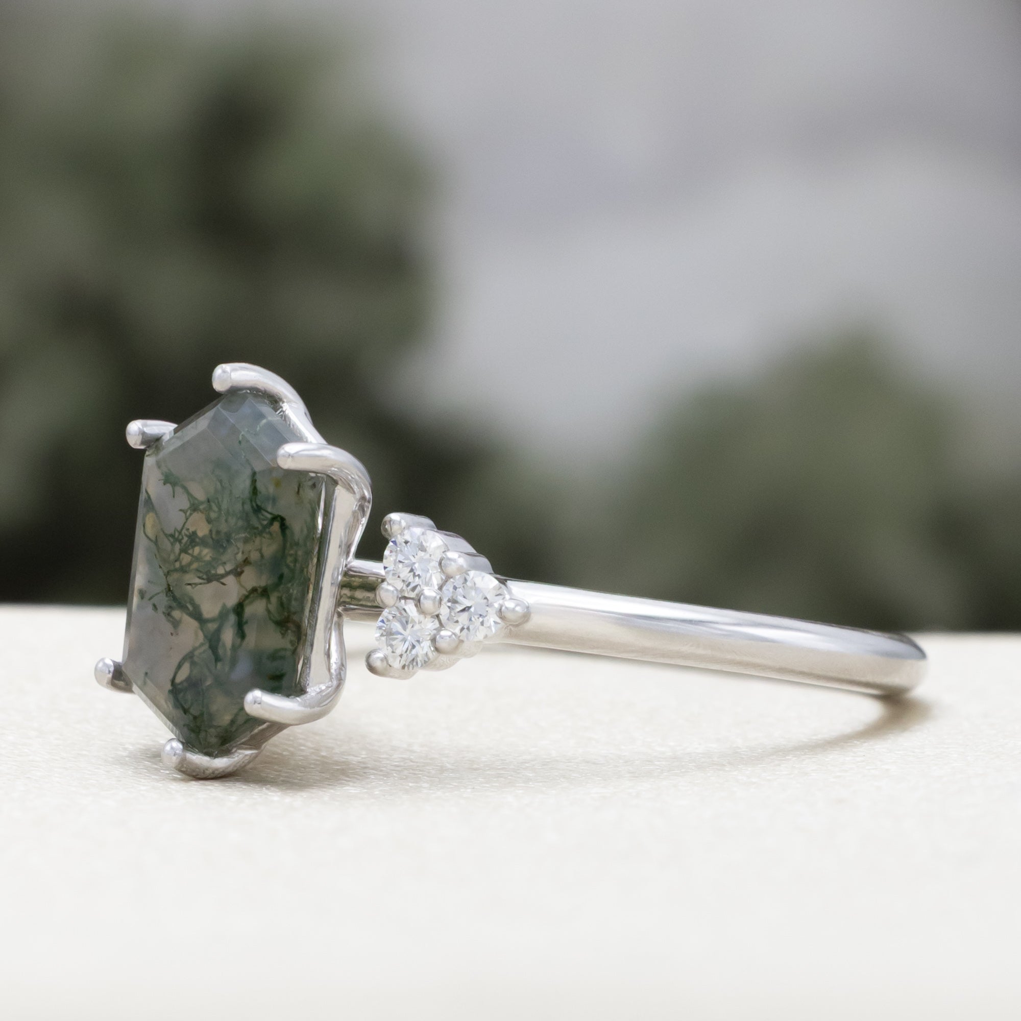 14K white gold engagement ring with moss agate on a blurred background