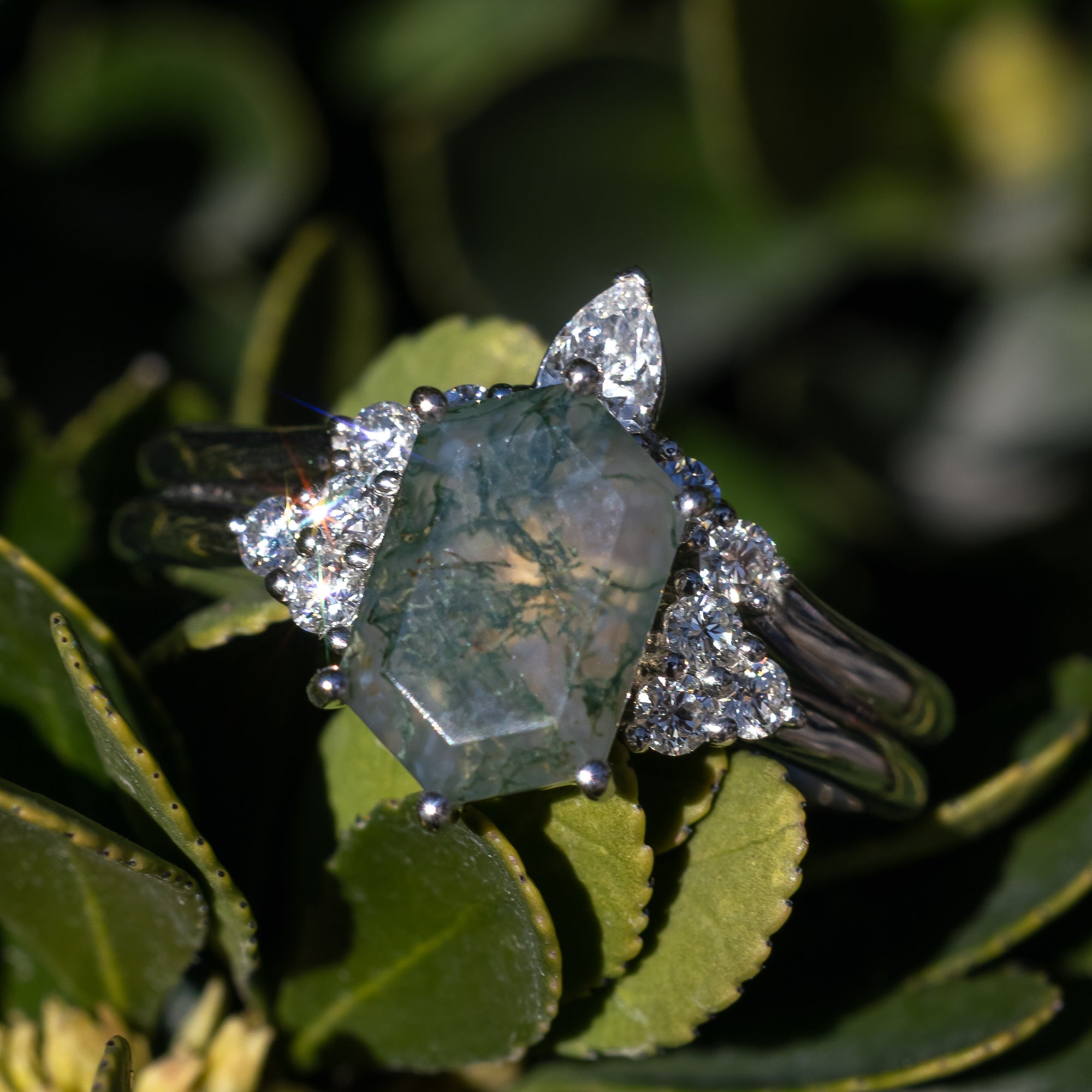 White gold engagement ring and tracer with moss agate and diamond accents on a blurred natural background